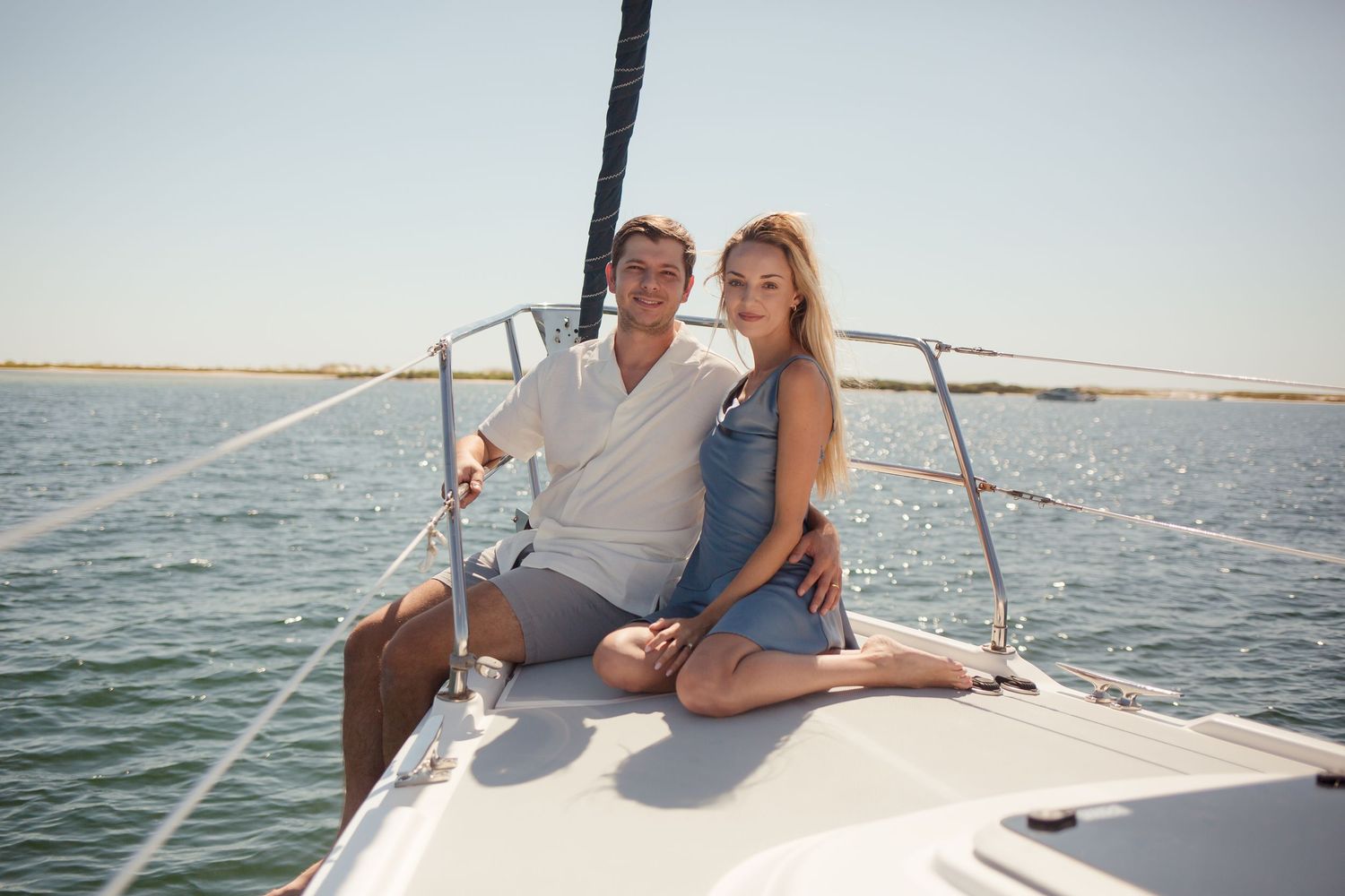 Smiling couple sitting together on the bow of a sailboat on a sunny day.