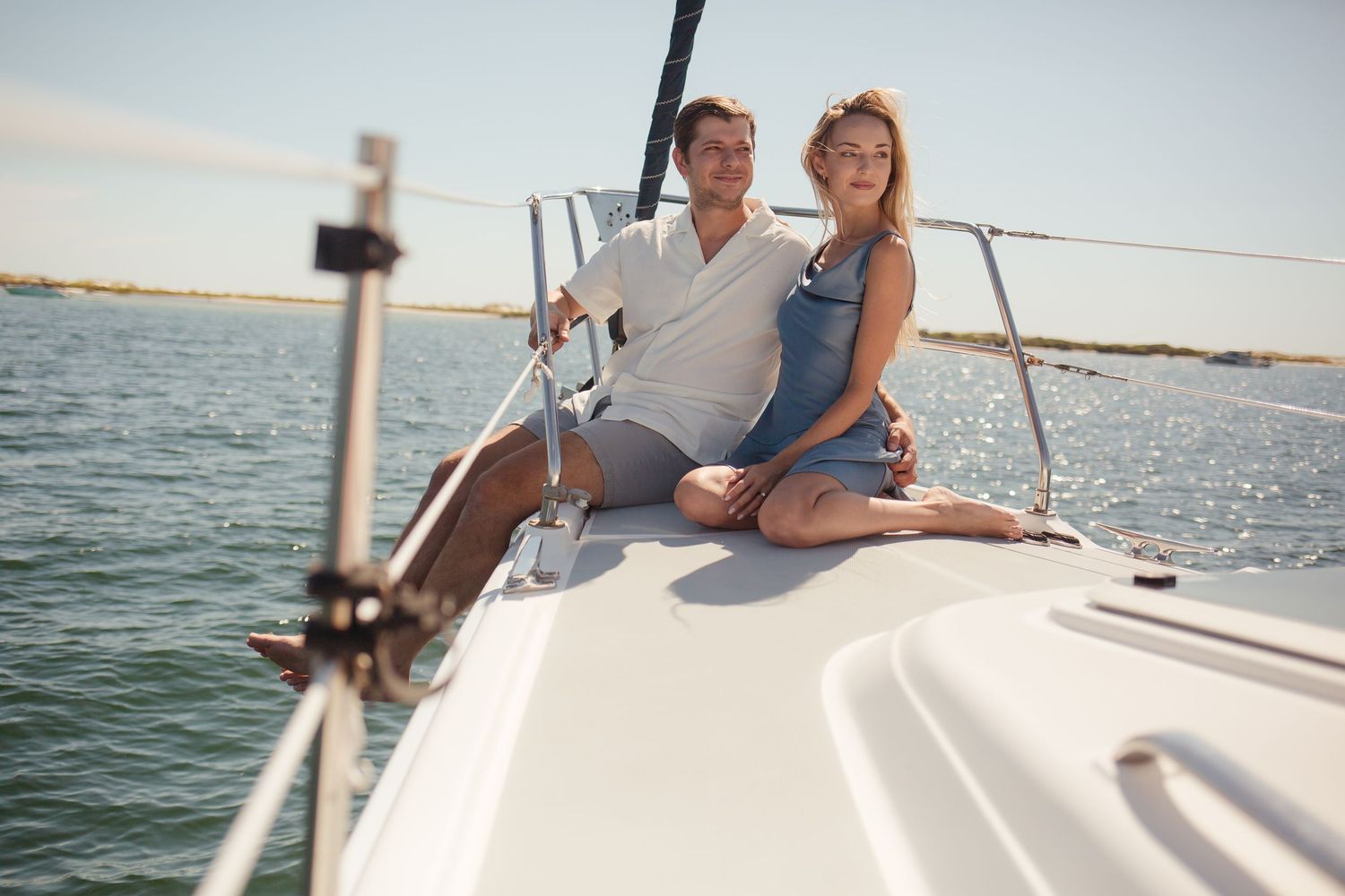Young couple sitting together on a white sailboat deck, enjoying a sunny day on the water.