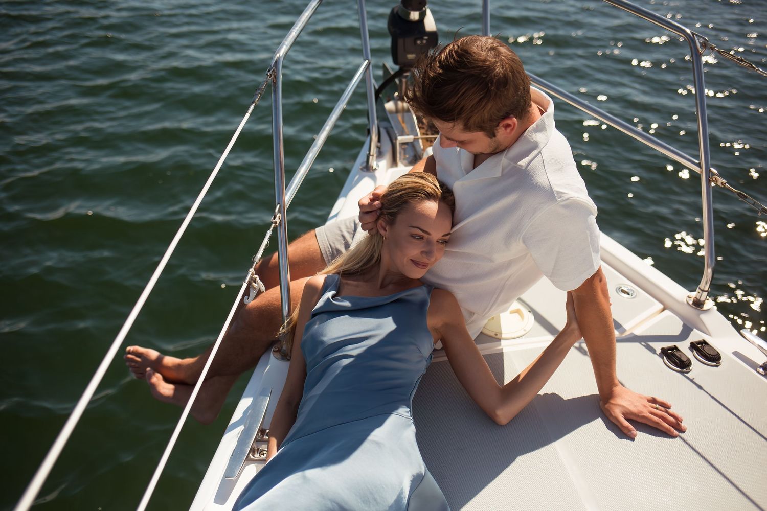 Couple sharing an intimate moment on a sailboat deck surrounded by sparkling blue water.