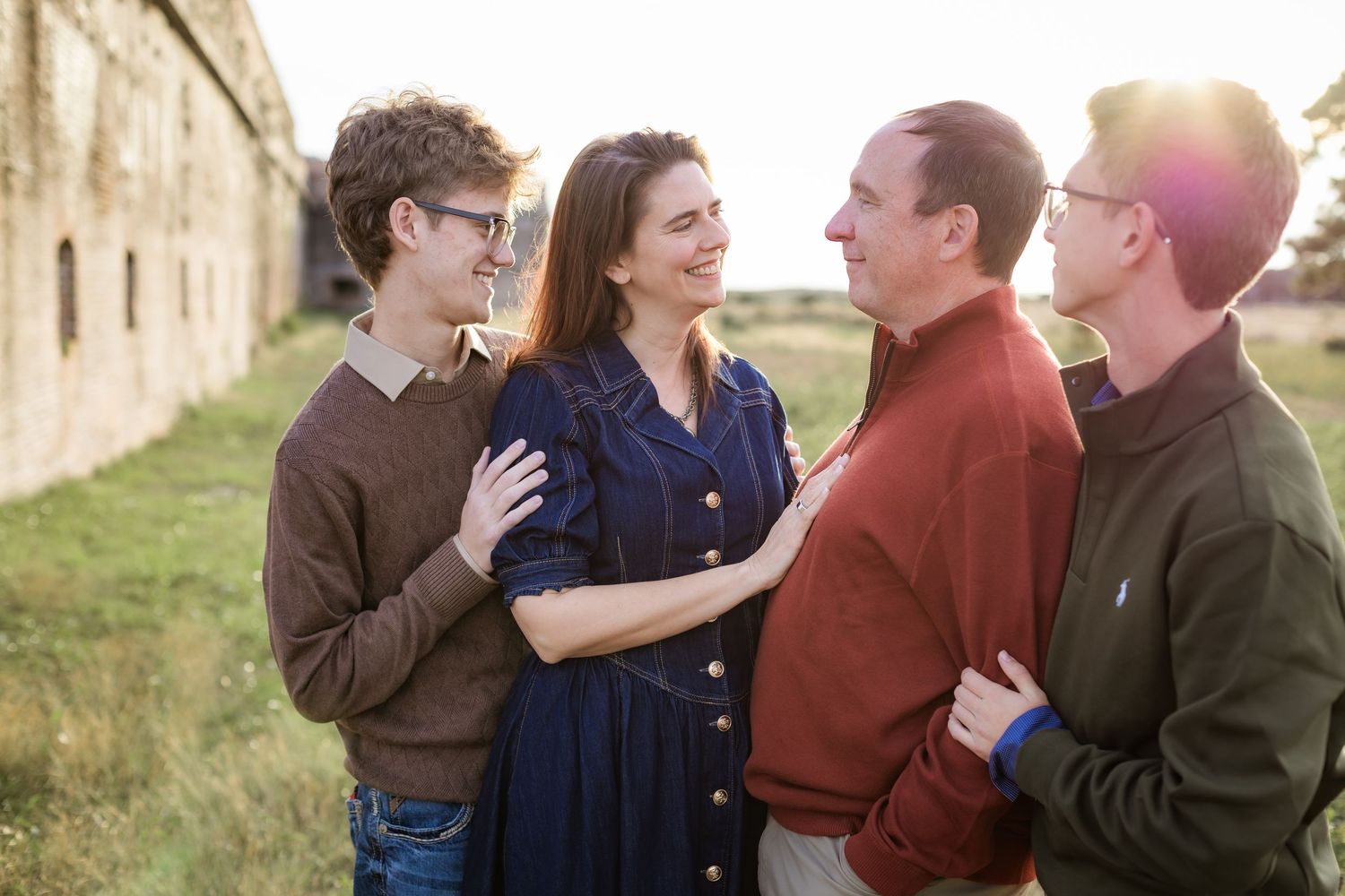 family smiling at each other near brick wall in the sunshine