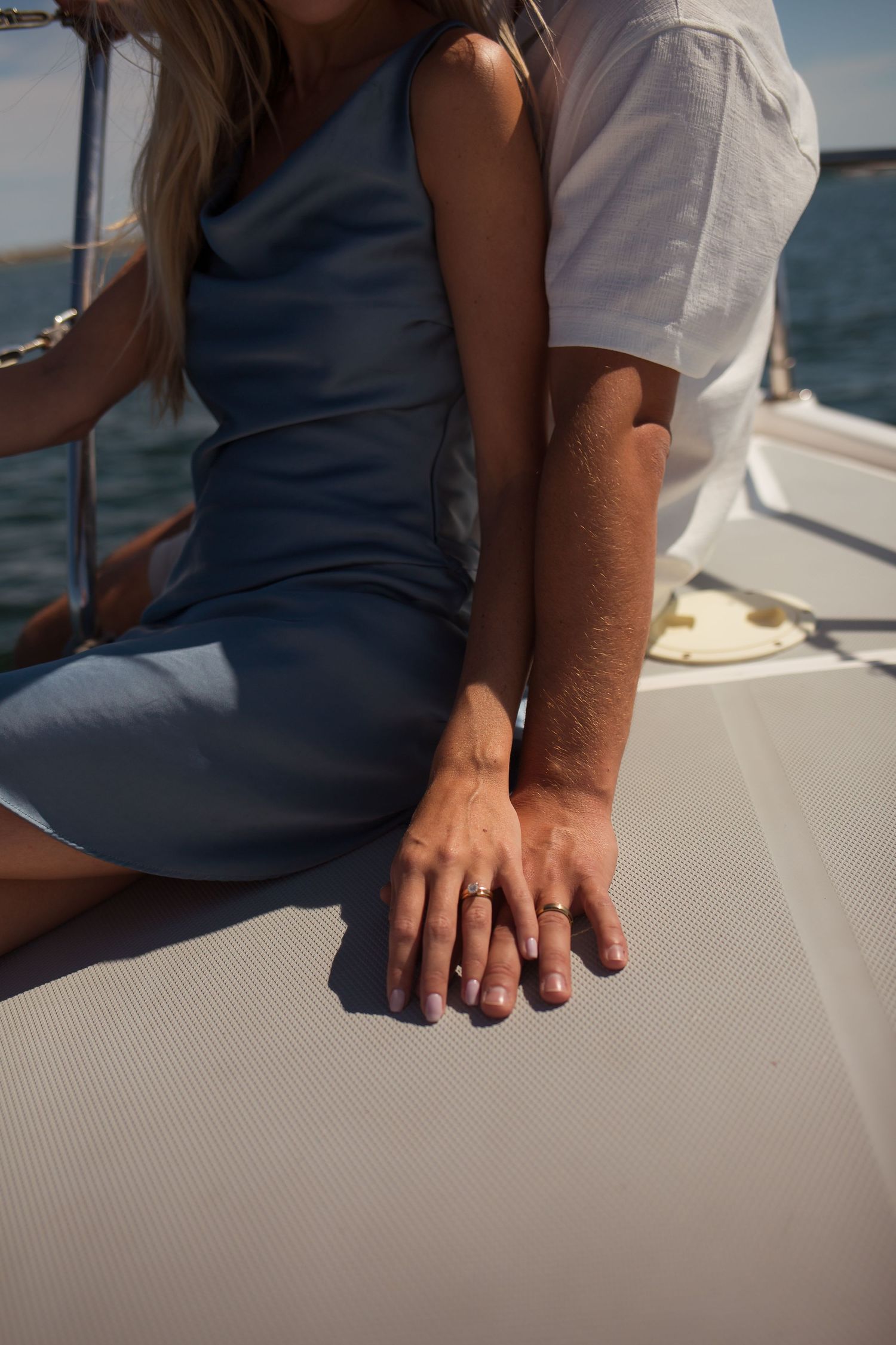 Close-up of couple's hands with wedding rings resting together on a white yacht deck.
