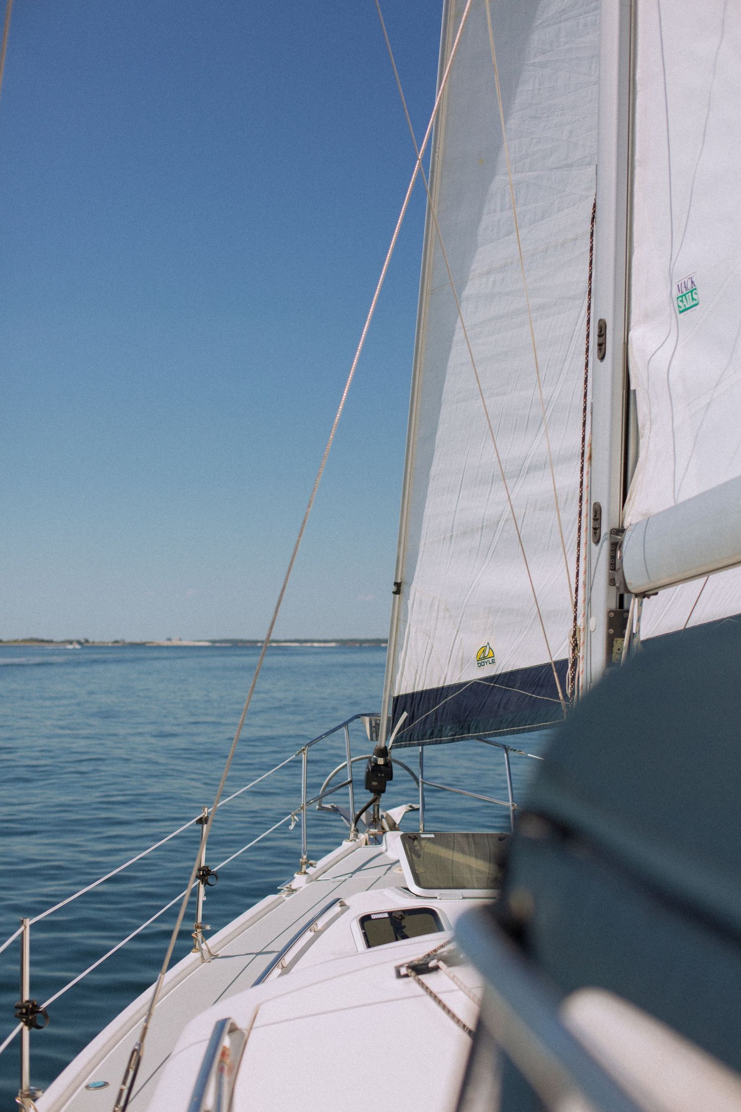 White sailboat sail billowing against a clear blue sky on calm open water.