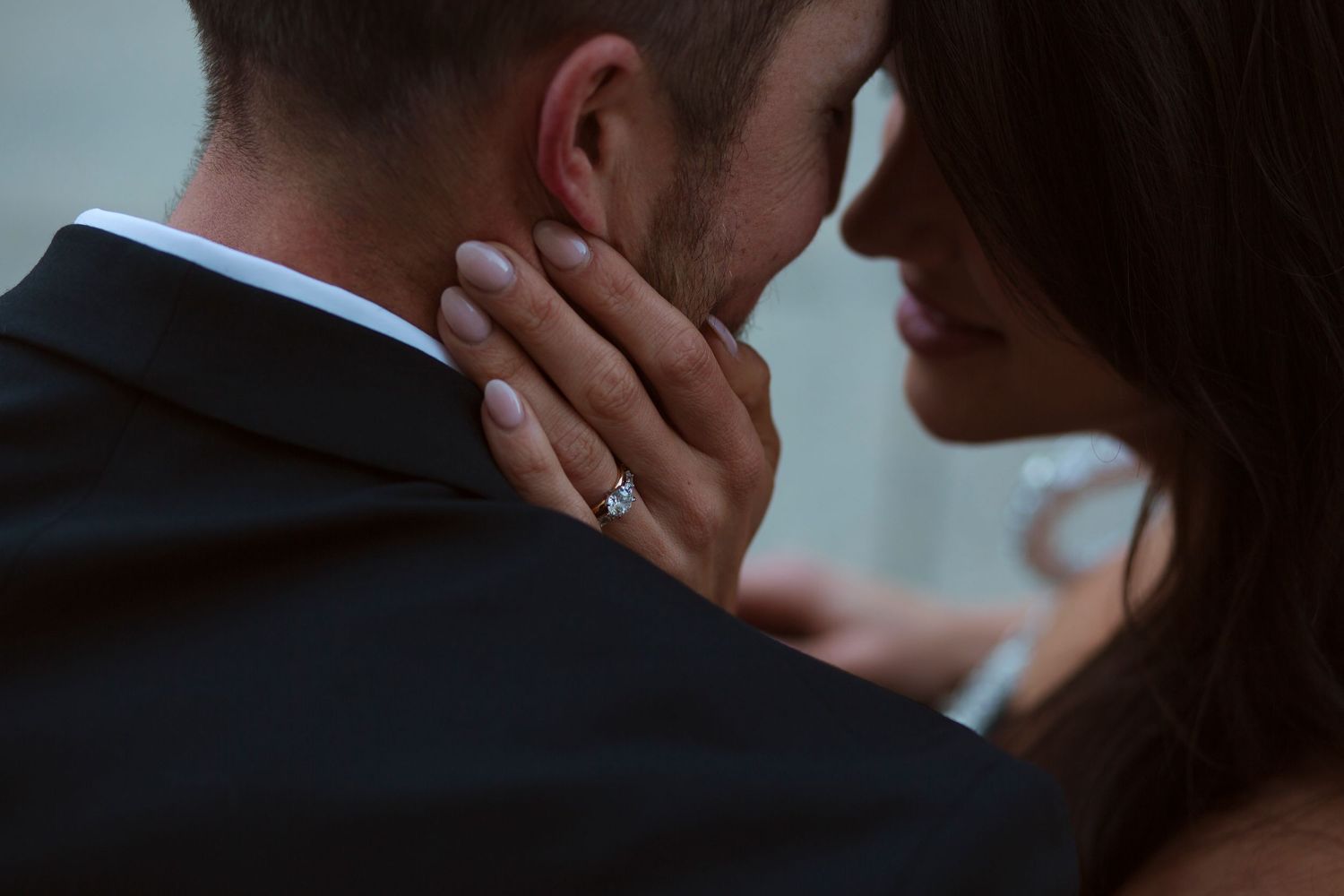 Close-up of a bride resting her hand on a groom's neck, showcasing a diamond engagement ring.