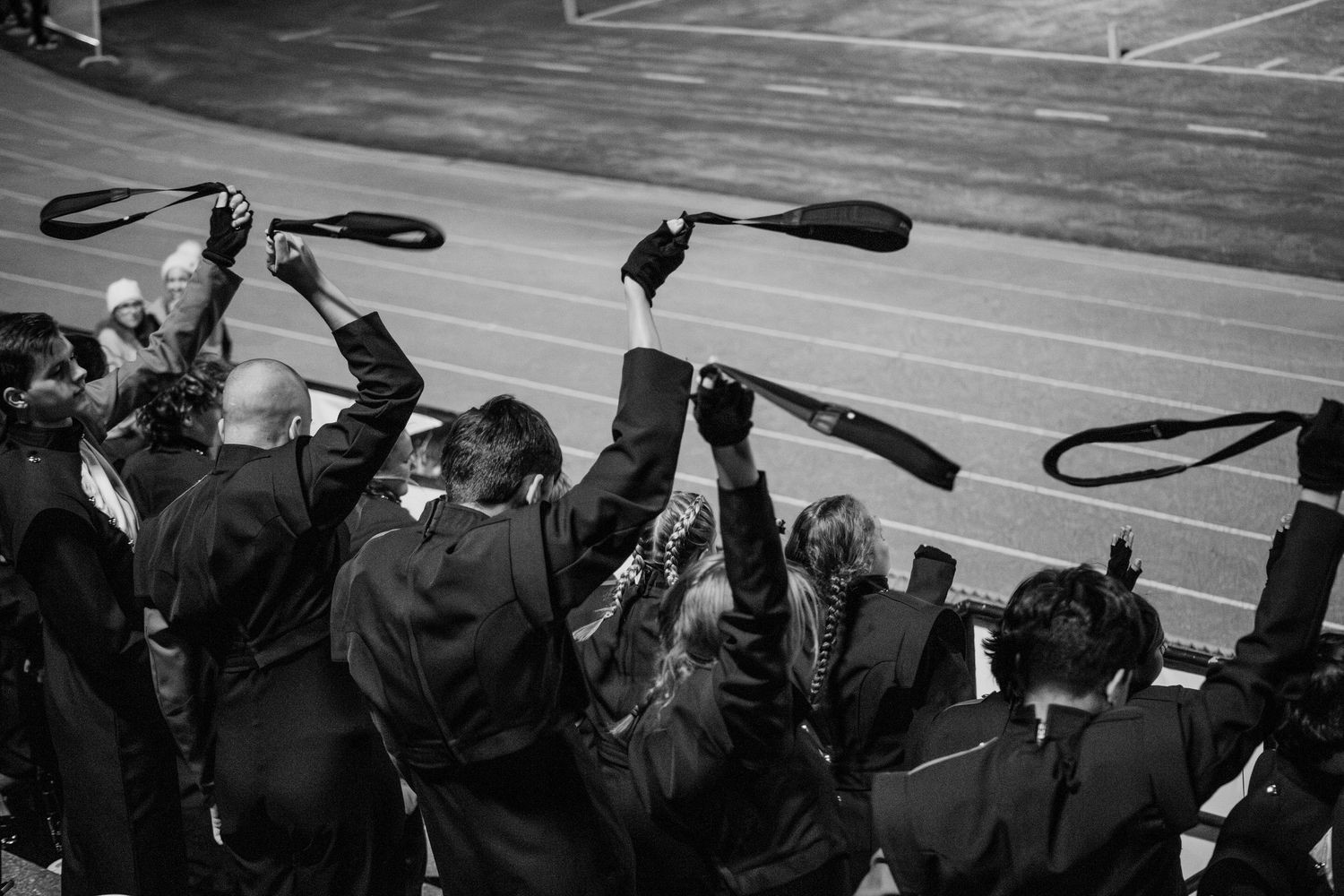 Graduates in black robes raise their caps in celebration at a track and field stadium during a commencement ceremony.