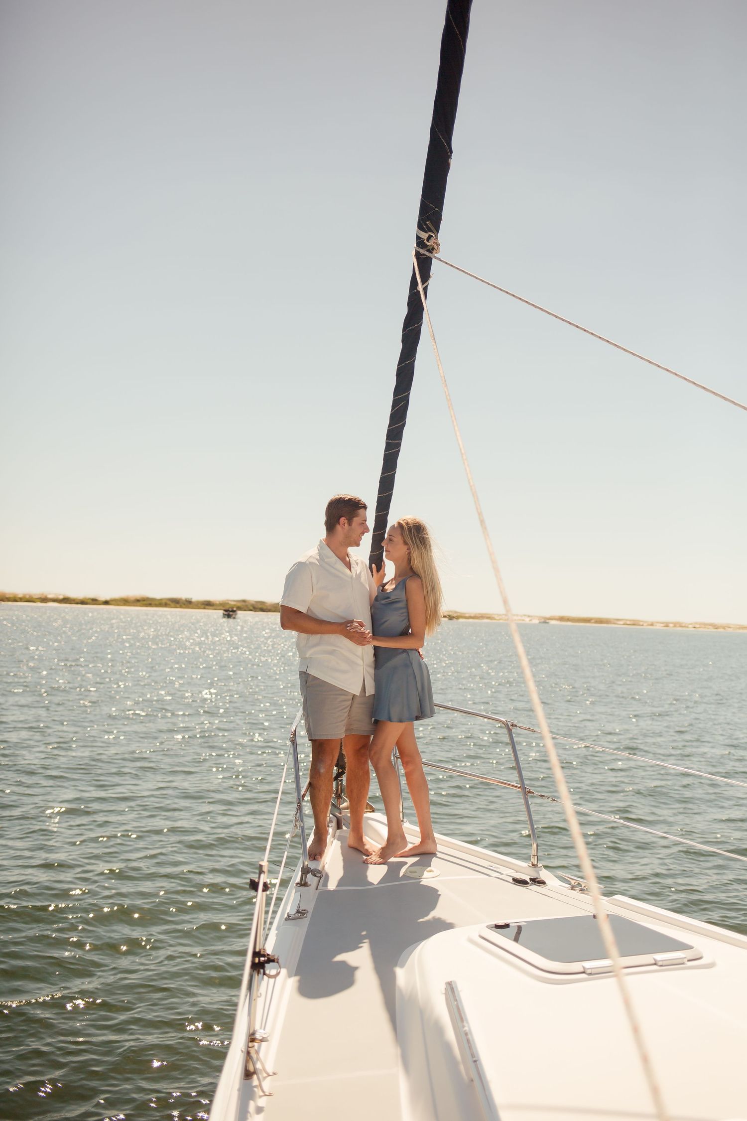 Romantic couple embracing on the bow of a sailboat on sparkling sunlit water.