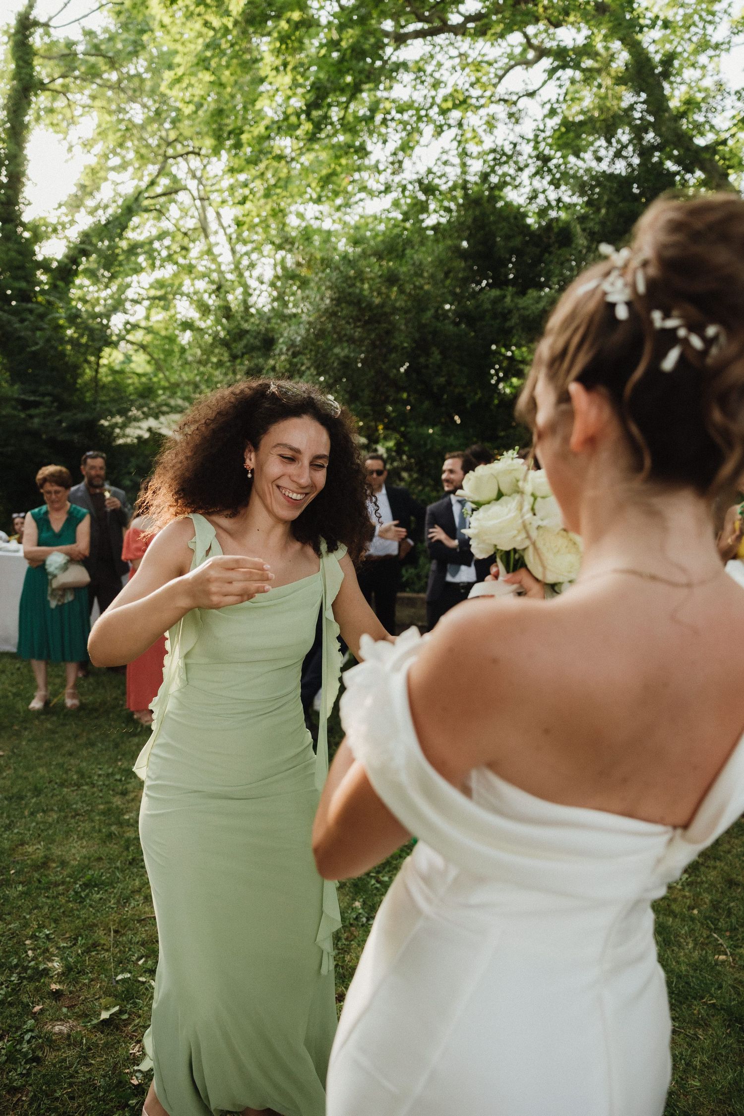 Wedding party members in white and mint green dresses dancing outdoors under trees.