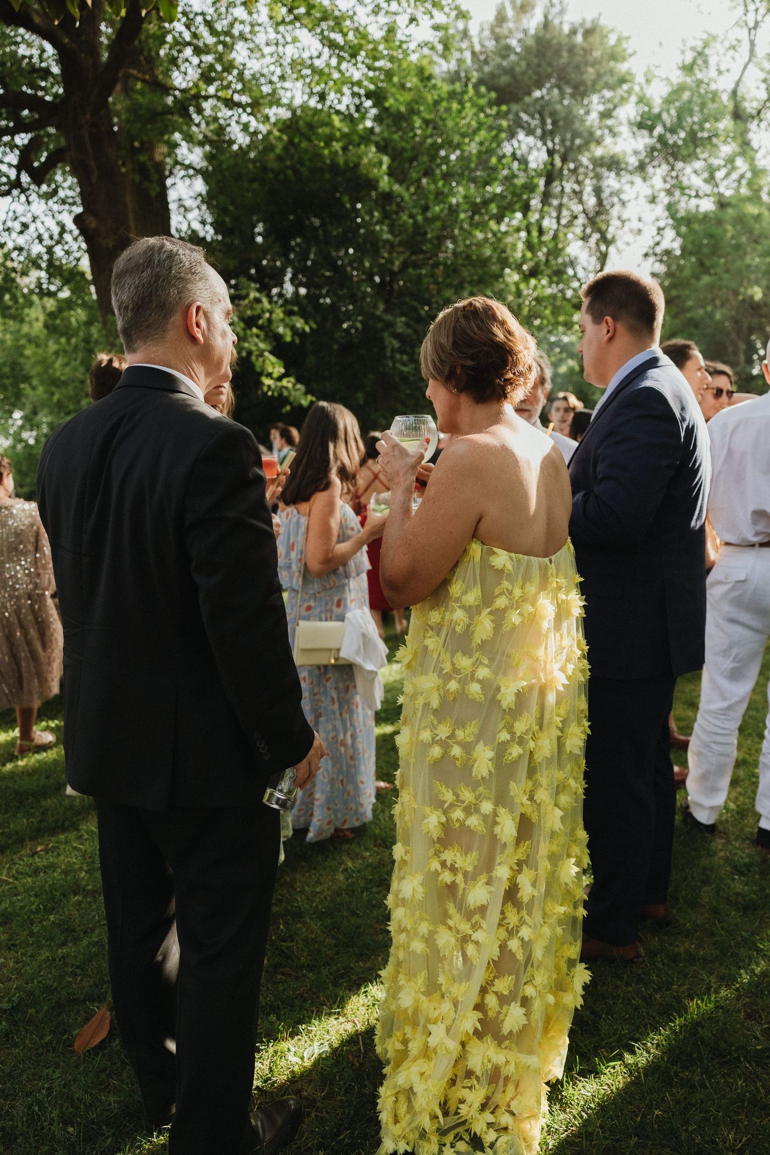Wedding guests socialize in garden setting during golden hour.
