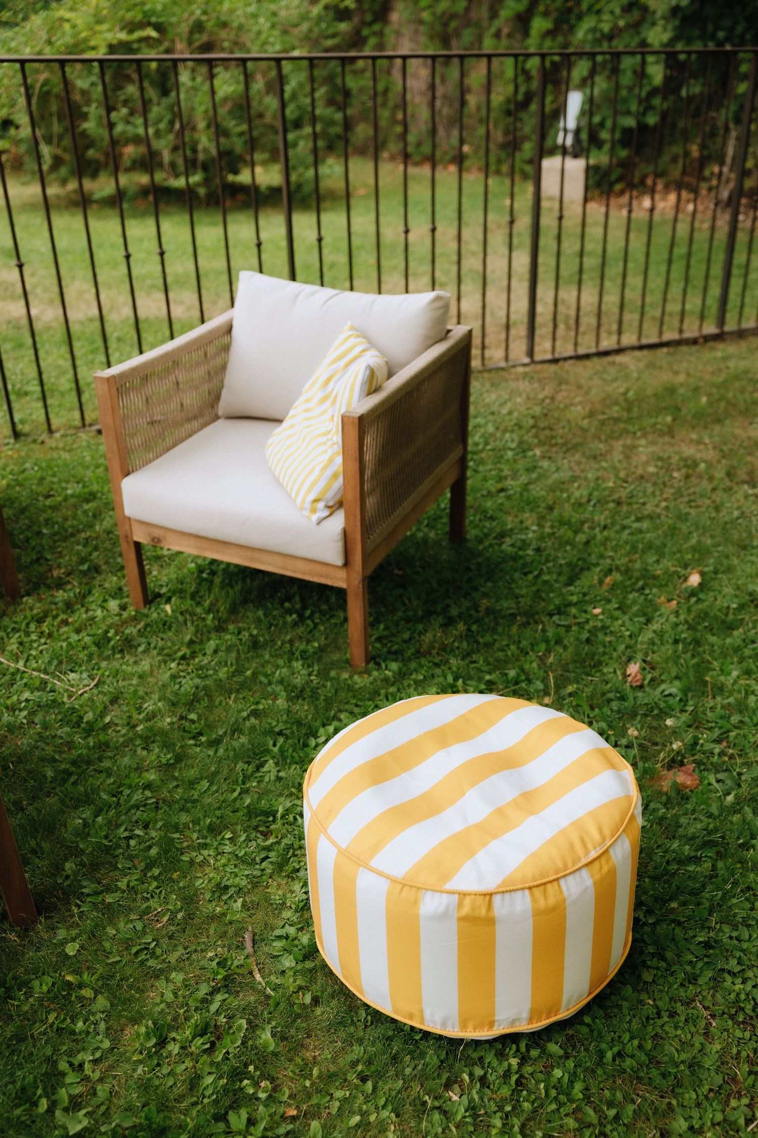 Outdoor lounge setup with wooden bench and yellow striped poufs on green lawn.