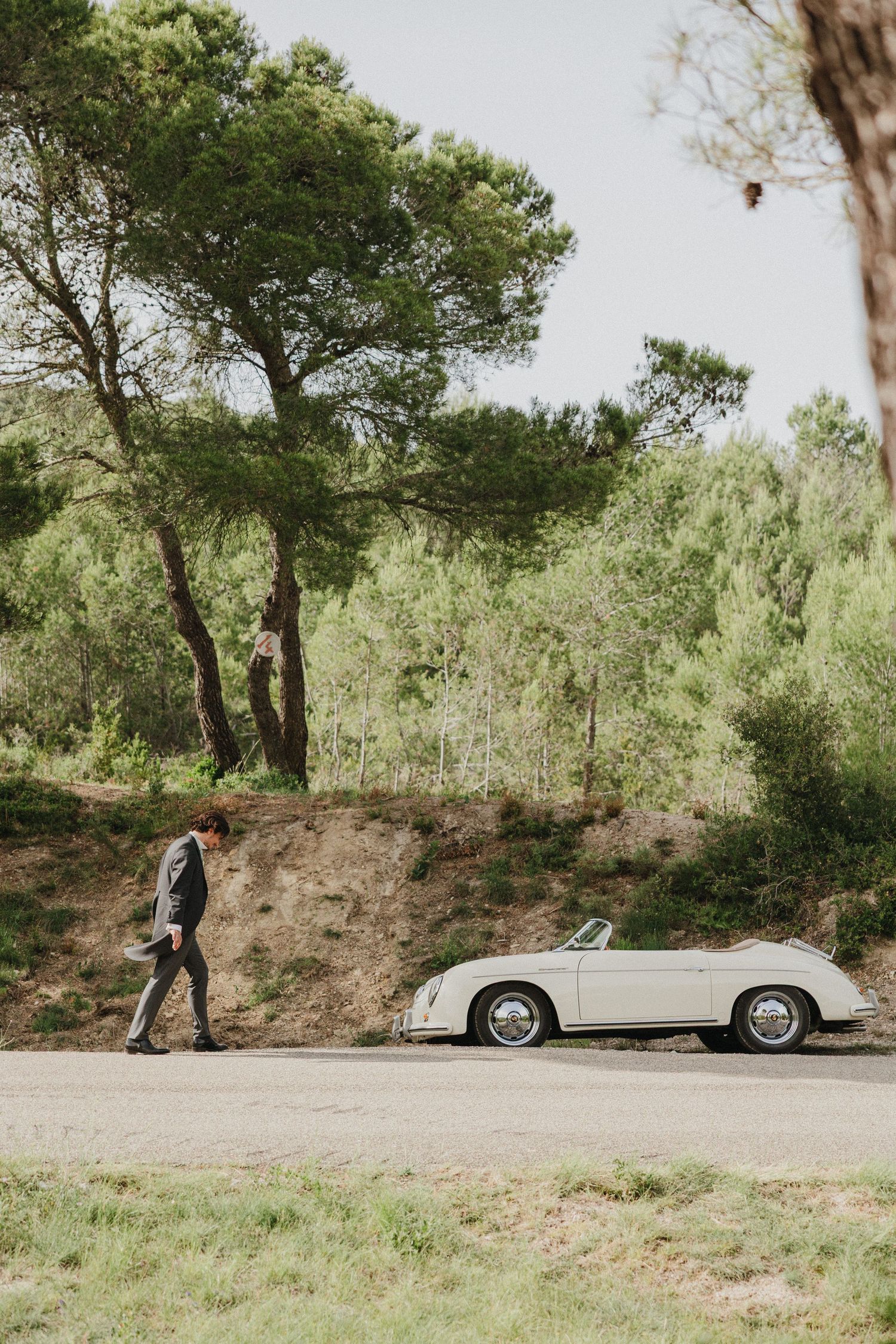 Classic convertible car parked on a winding road surrounded by green trees and natural landscape.