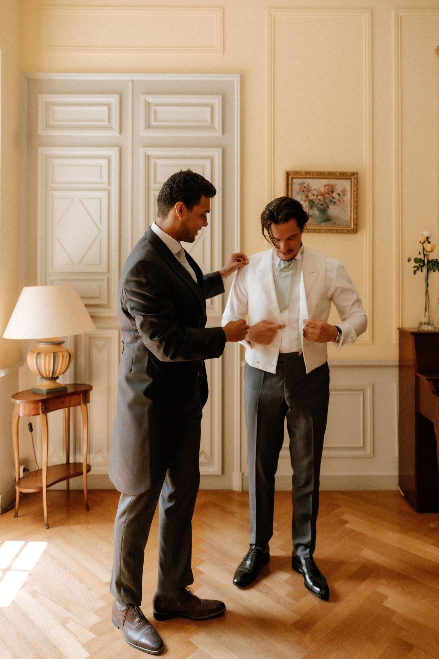 Sequence of men getting ready in a bright elegant room with white paneled walls and hardwood floors.