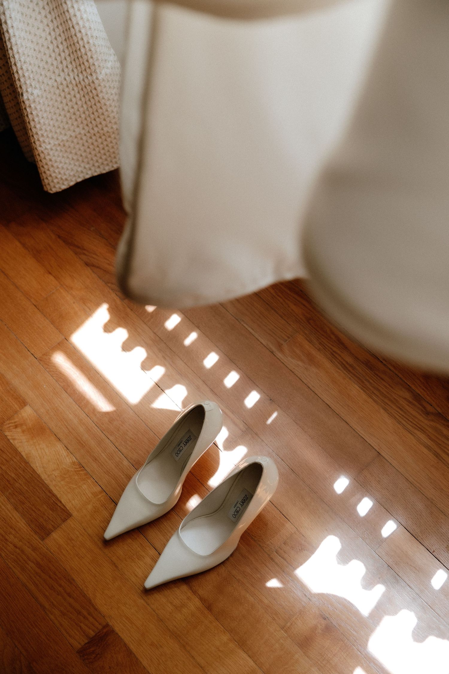 White bridal shoes on hardwood floor with sunlight casting geometric shadows.