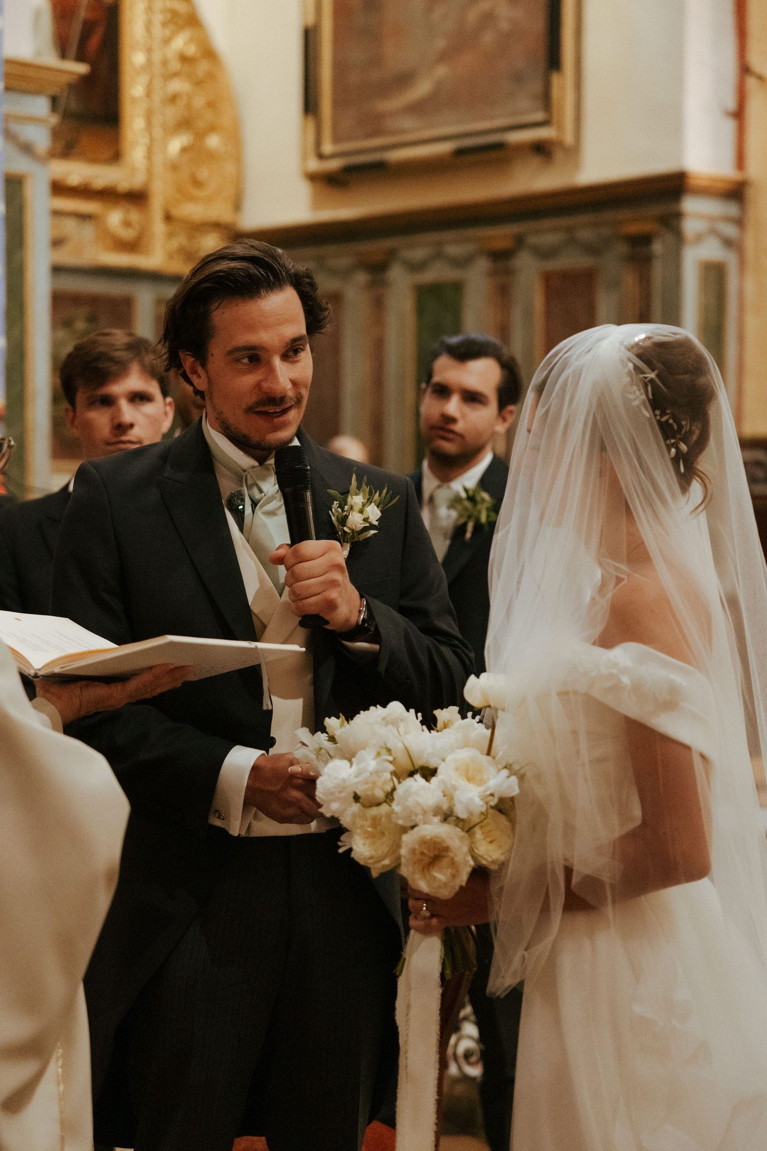 A wedding ceremony in a church with the couple exchanging vows while holding white flowers.