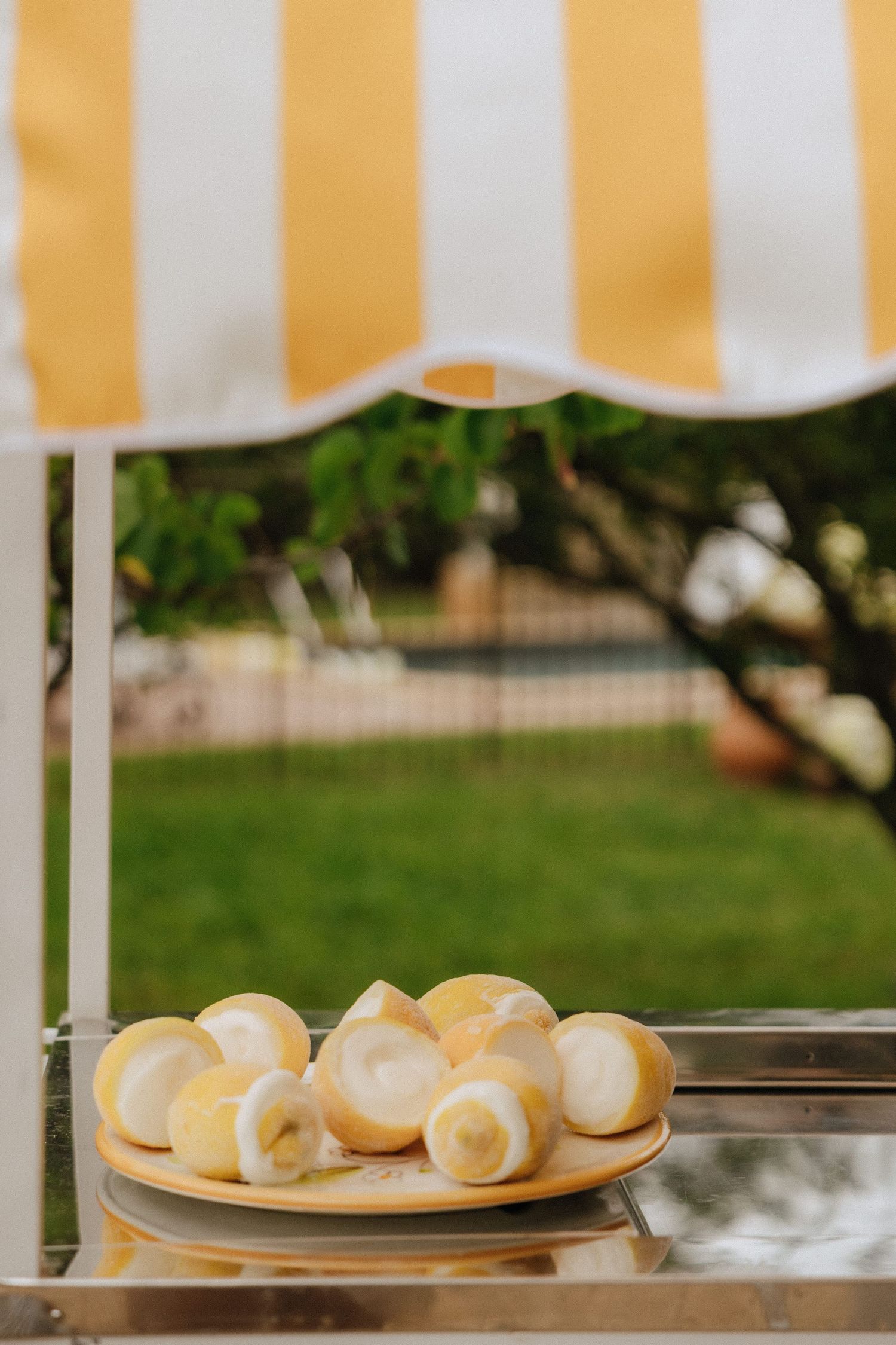 Fresh bread rolls displayed on plate under yellow and white striped awning outdoors.