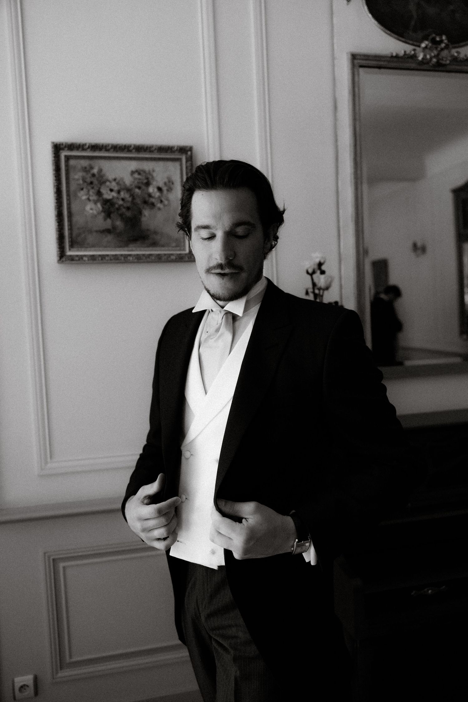 A black and white portrait series showing a man in formal attire against a white wall with artwork.