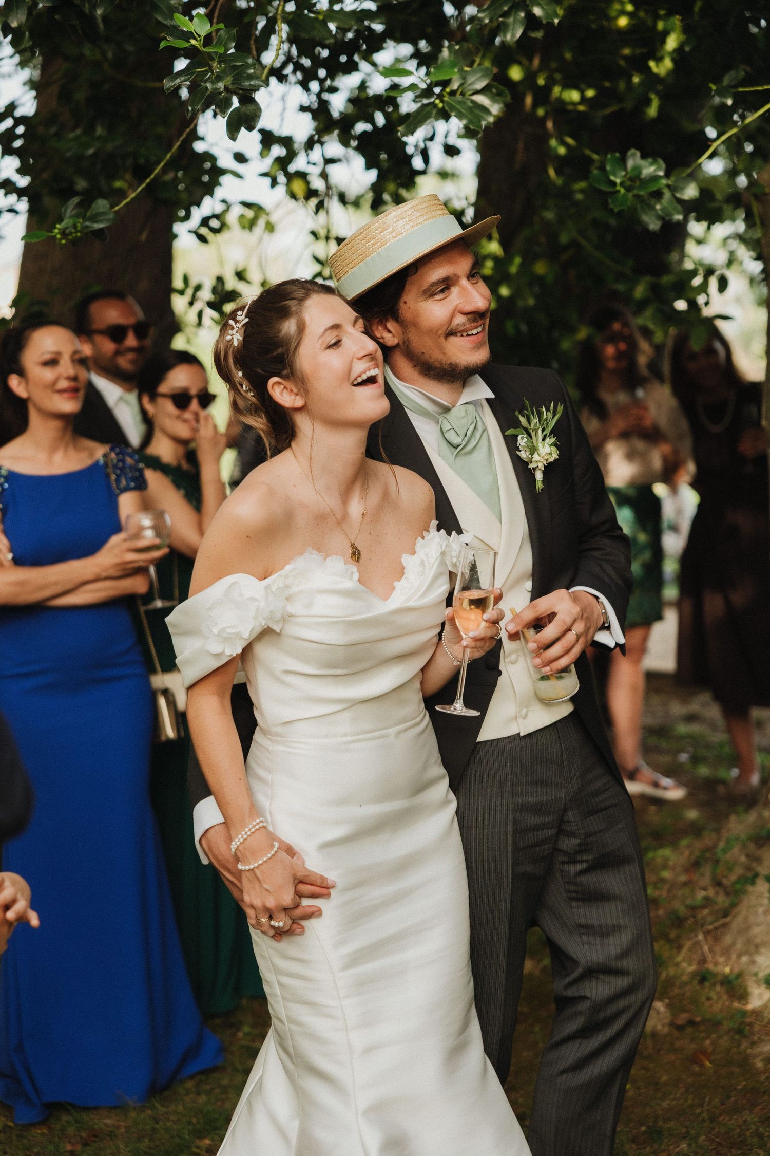 A joyful wedding celebration outdoors with guests in formal attire under green trees.