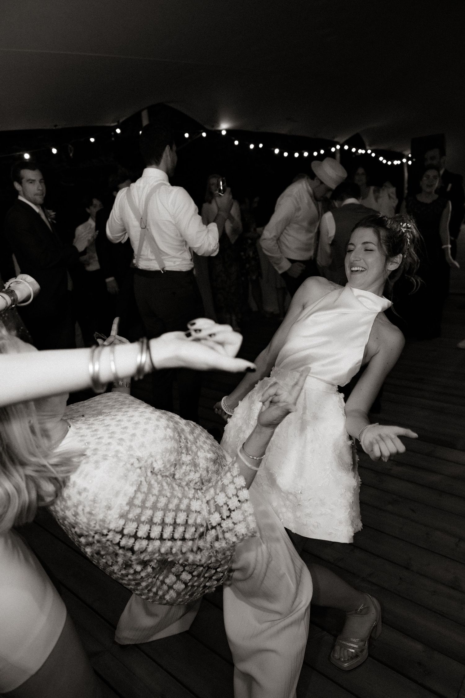 Lively dance floor scene at a wedding reception with string lights overhead in black and white.