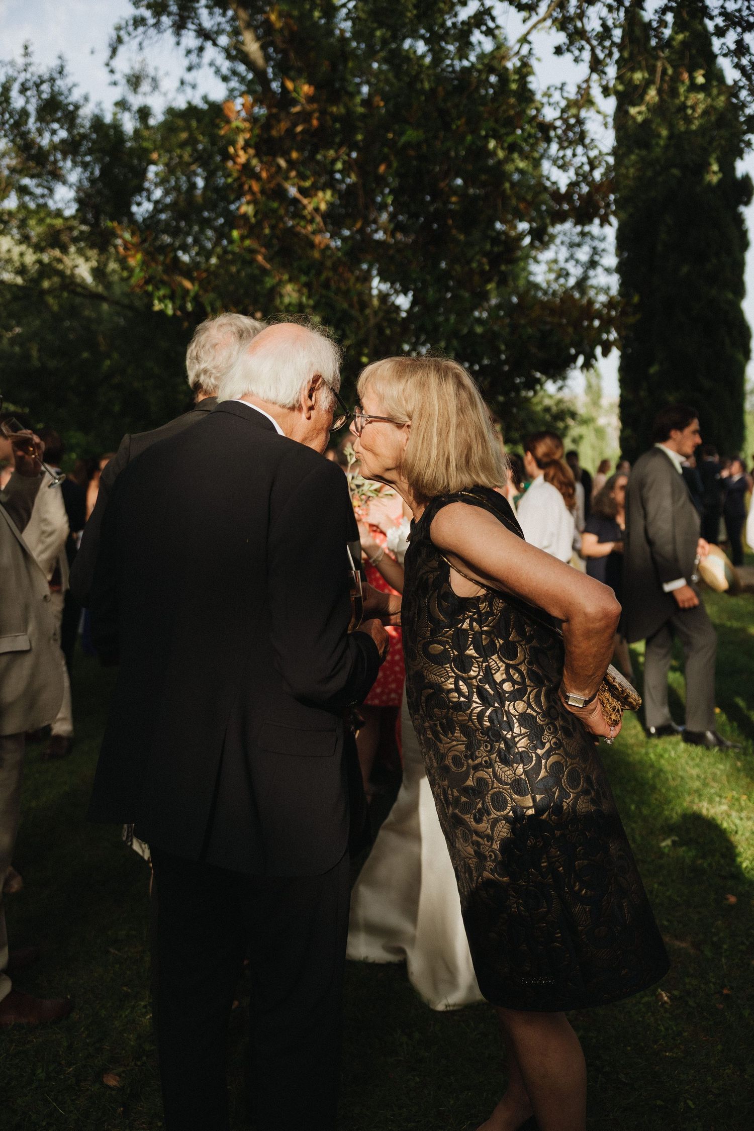 Wedding guests mingling at an outdoor evening reception under trees.