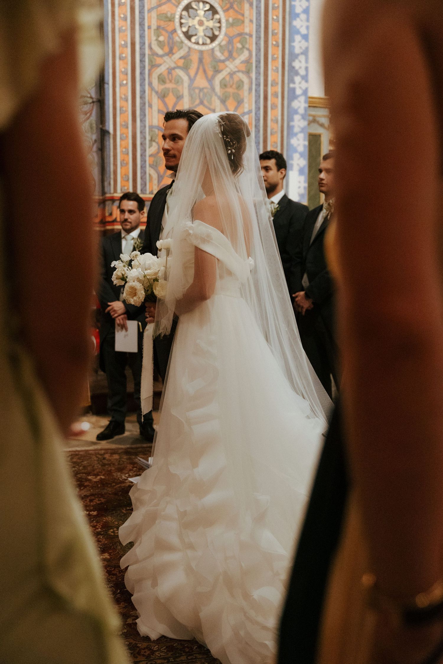Bride in flowing white gown walking down ornate church aisle during wedding ceremony.