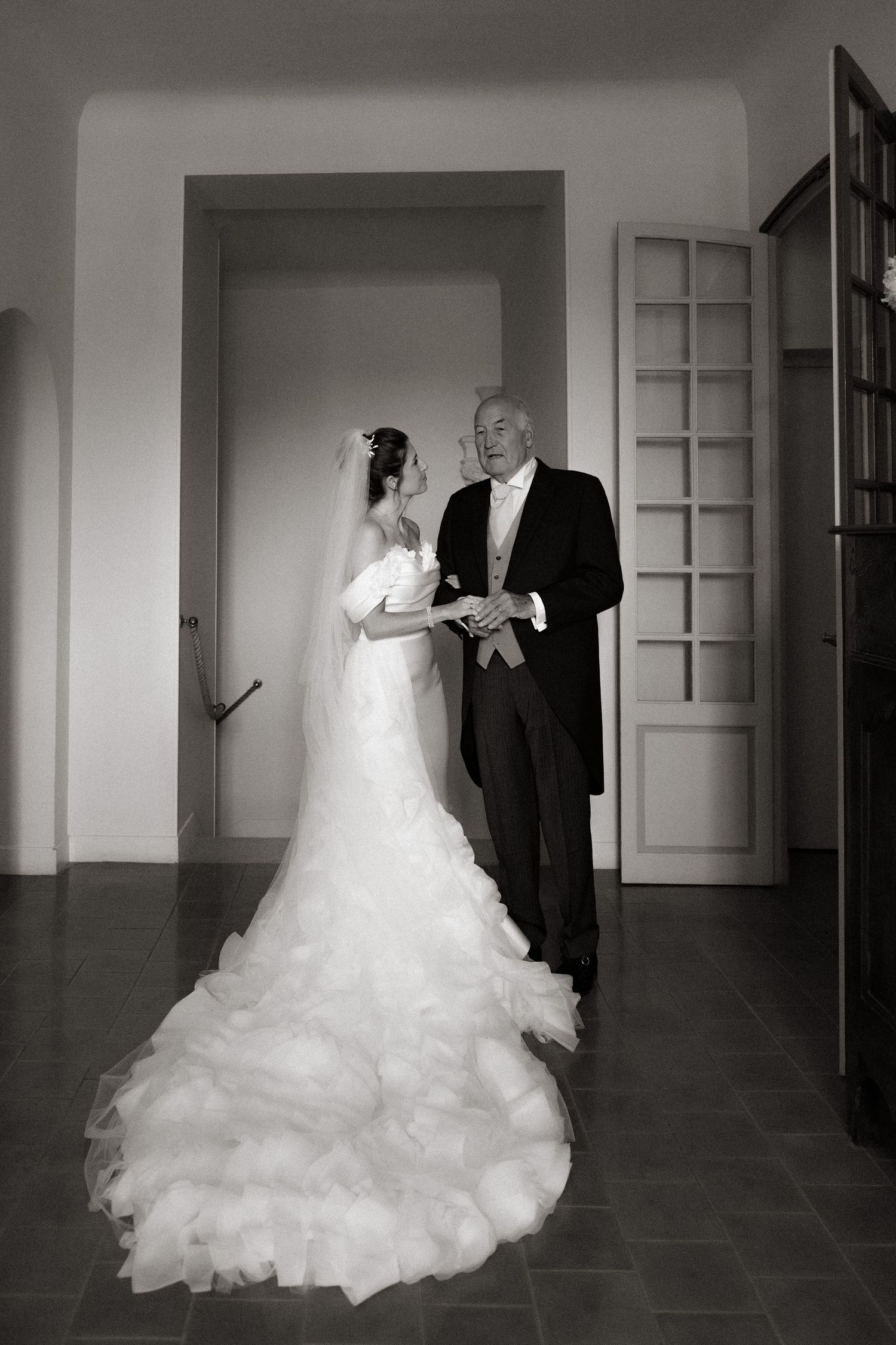 Black and white photos capture a bride in a dramatic wedding gown walking through an elegant corridor.