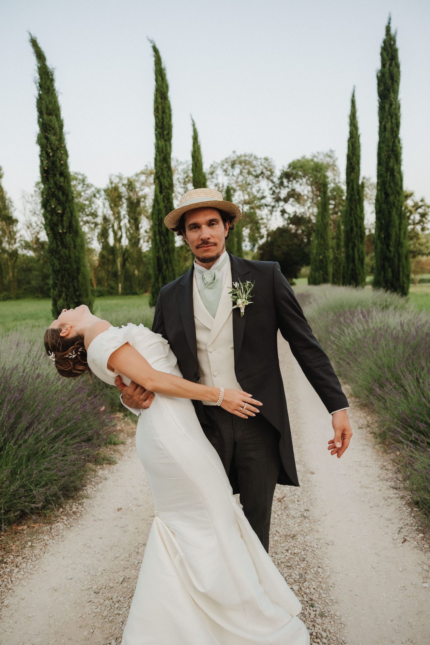 Wedding couple poses along a cypress-lined path in a romantic garden setting.