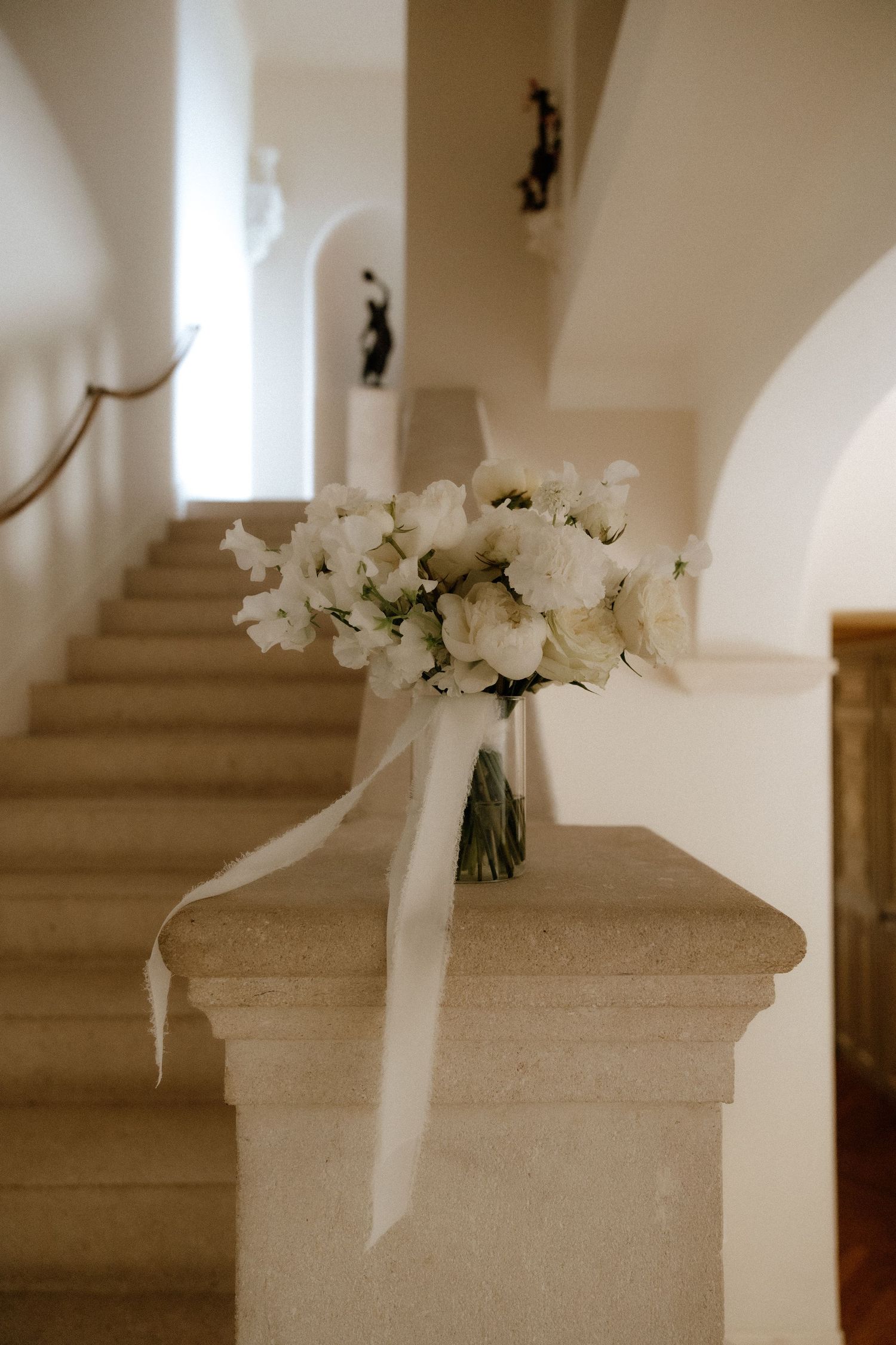White wedding bouquet rests on a beige stone ledge in a minimalist architectural setting.
