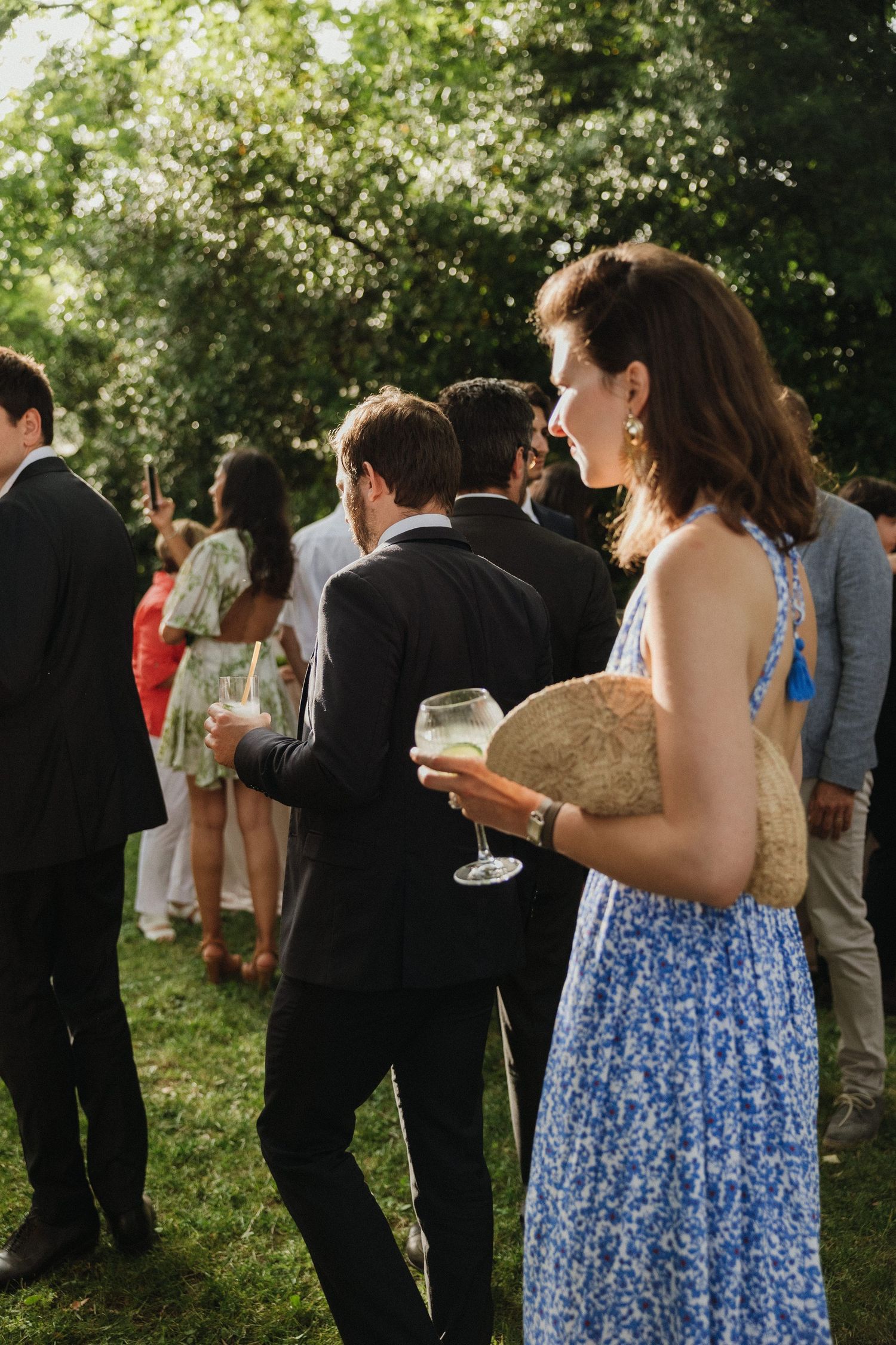 Wedding guests mingle at outdoor garden reception with drinks.