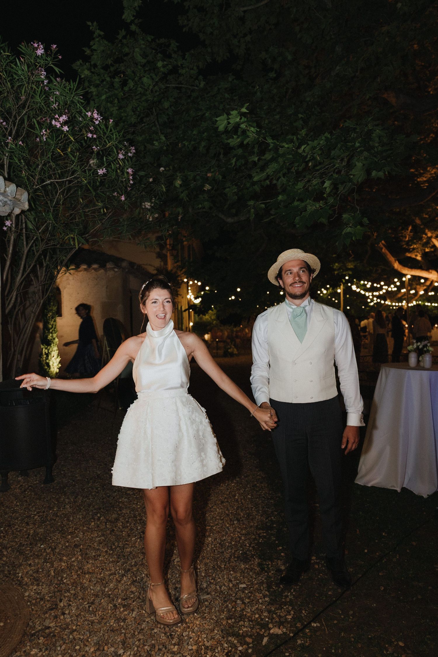 Wedding party dancing under string lights at an outdoor evening celebration.