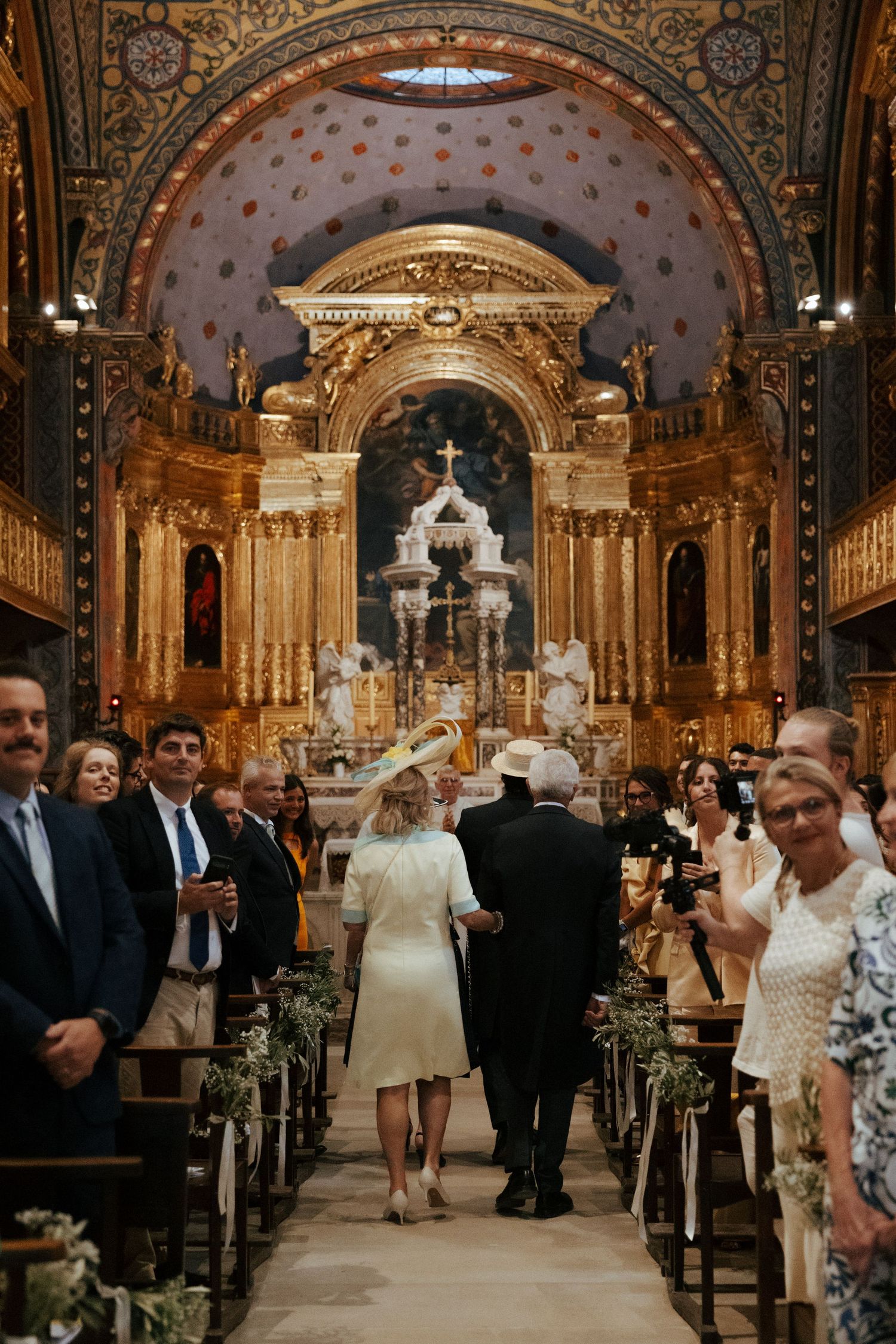 Wedding ceremony procession in an ornate cathedral with gilded decorations and arches.
