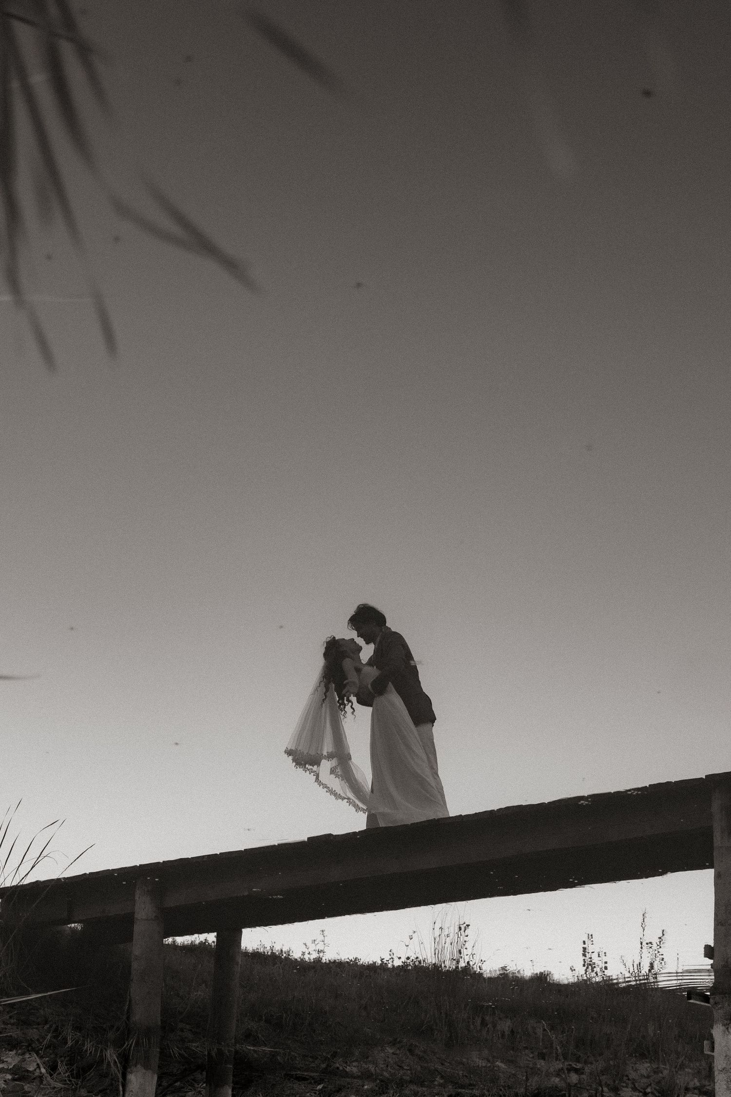 Black and white silhouette photograph of people holding cameras on a beam against a stark sky.