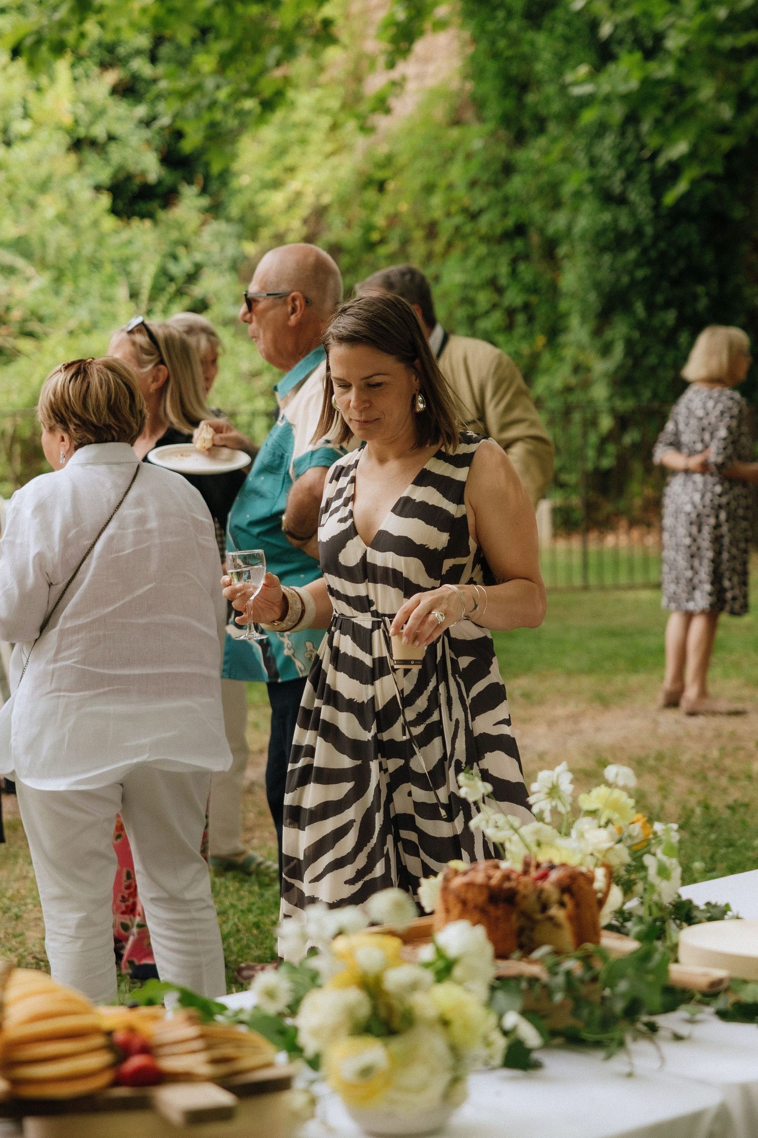 Guests enjoying food and drinks at an outdoor garden party buffet table with fresh decorations.