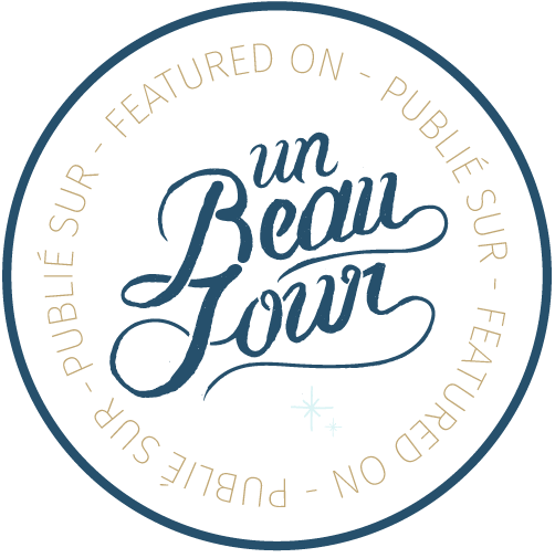 A circular logo badge with elegant blue script text reading 'un Beau Town' surrounded by curved text in a neutral color.