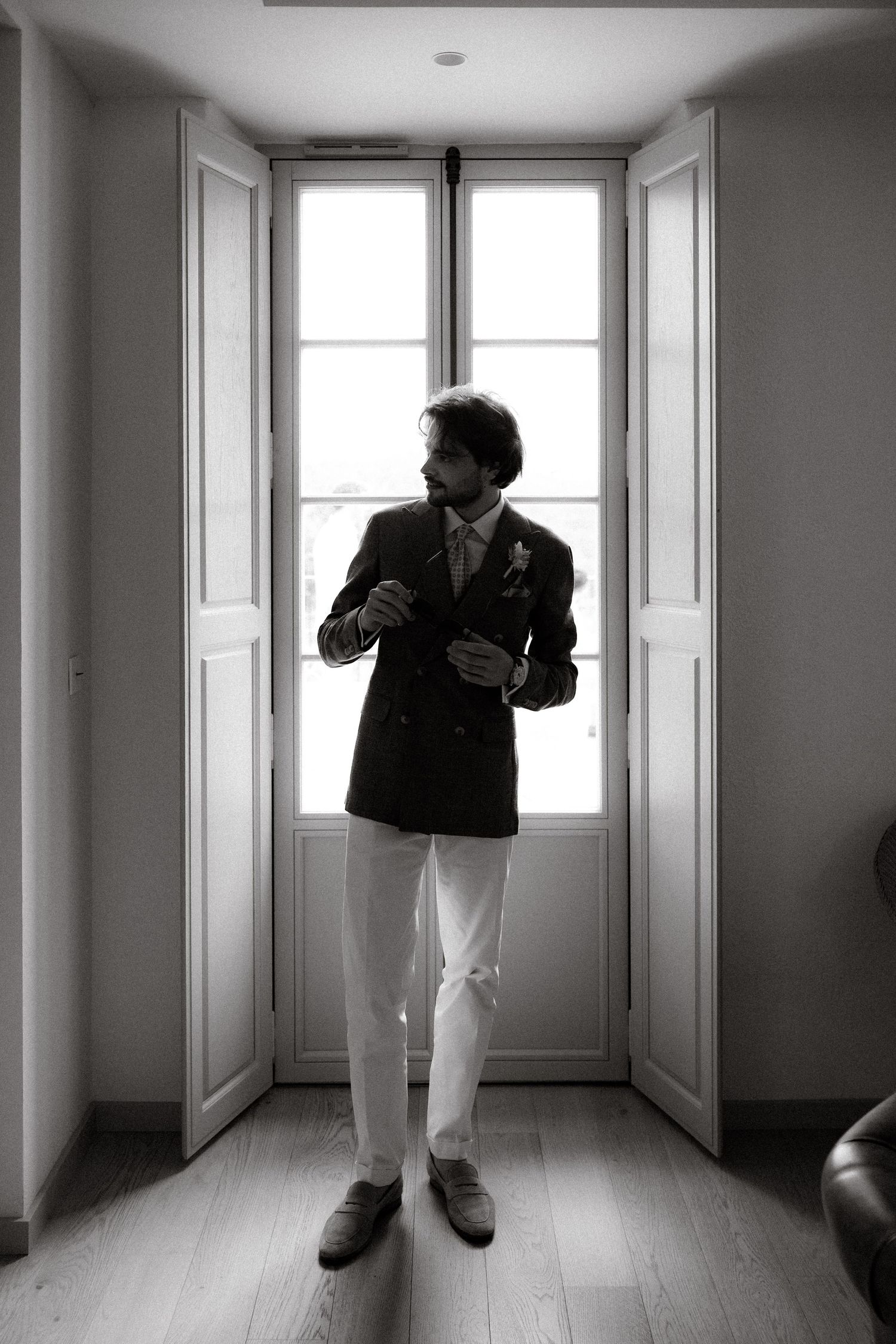 A black and white triptych shows a figure in a suit moving through an empty hallway with white walls and doors.