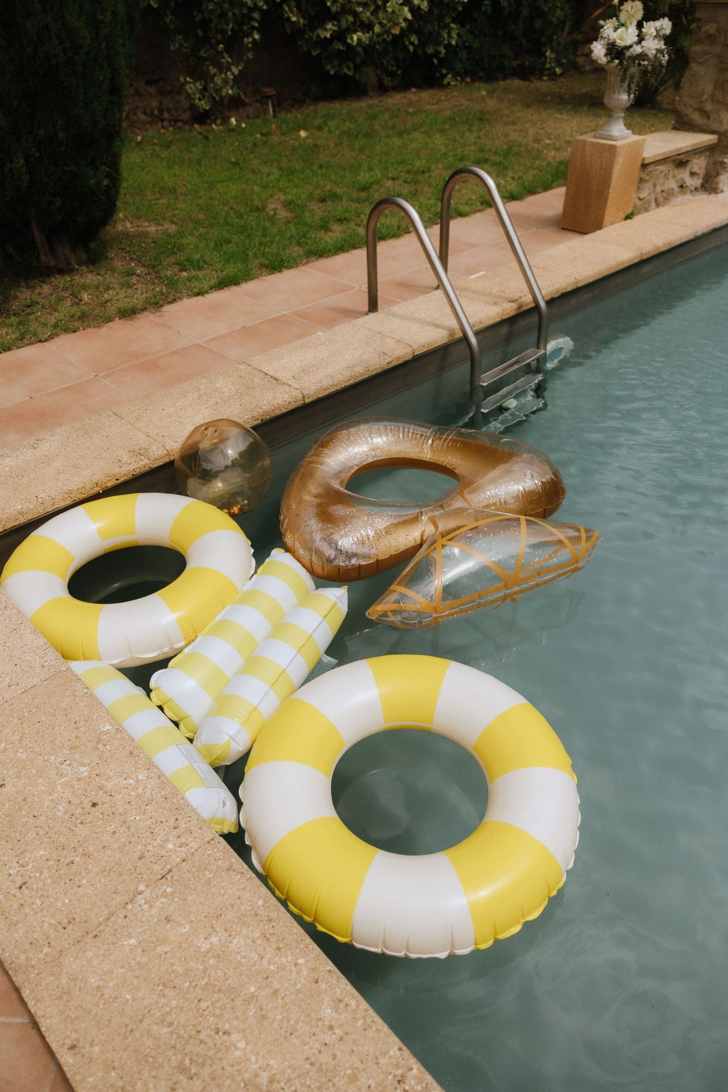Yellow and white striped pool floats rest beside a swimming pool at a summer party.
