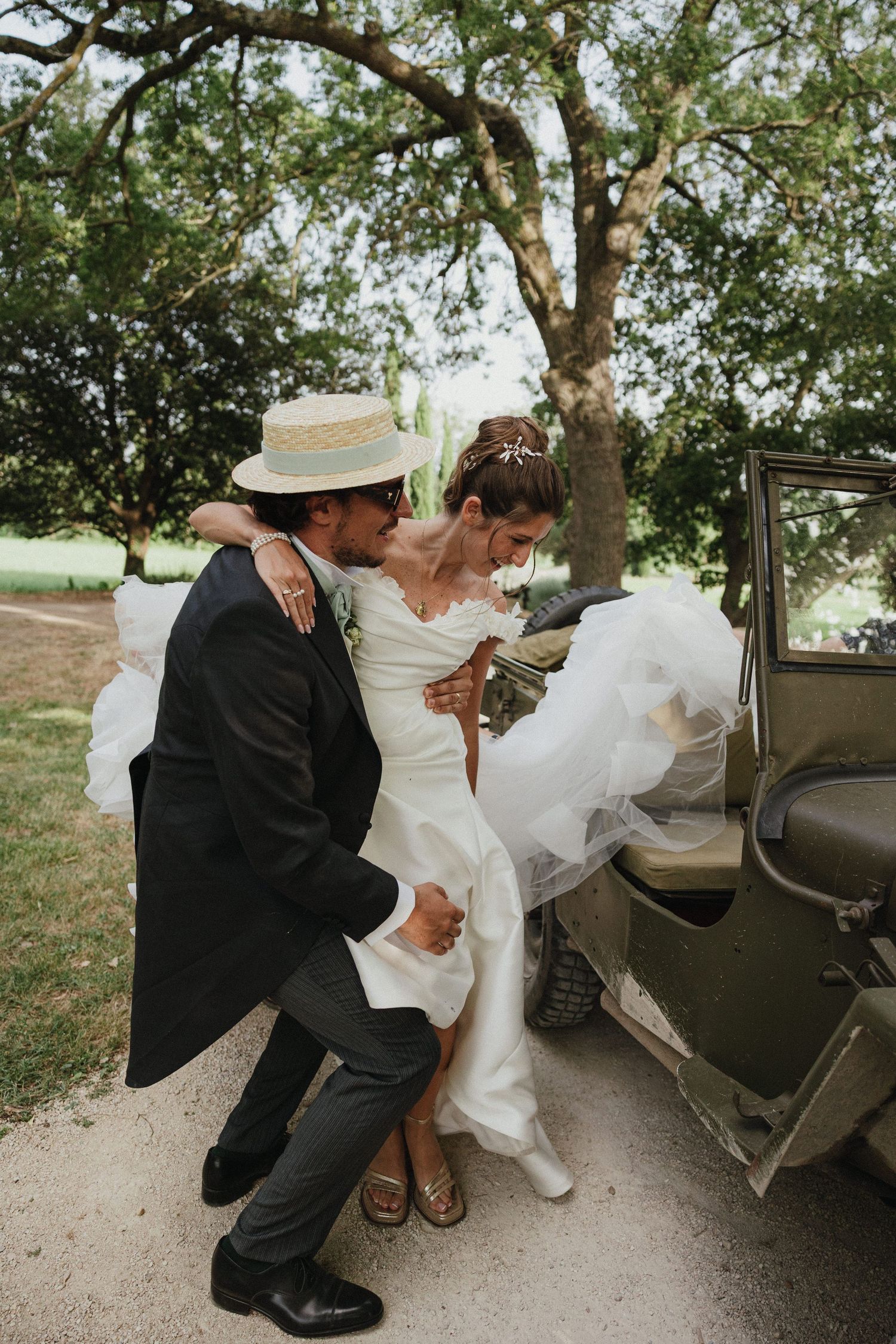 A couple in wedding attire helps the bride into a vintage car on their special day.