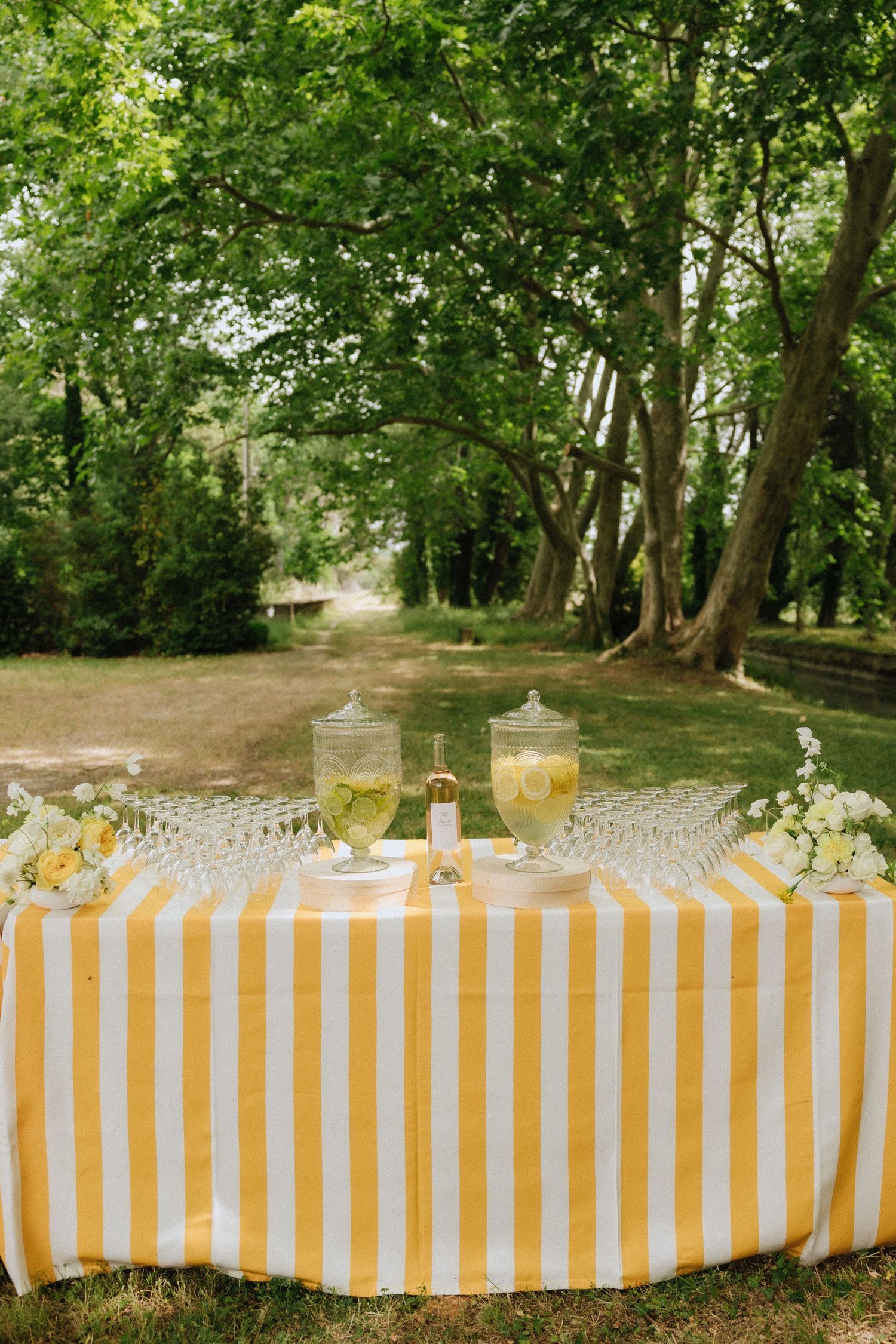 Yellow and white striped tablecloth with glass drink dispensers set up for an outdoor garden party.