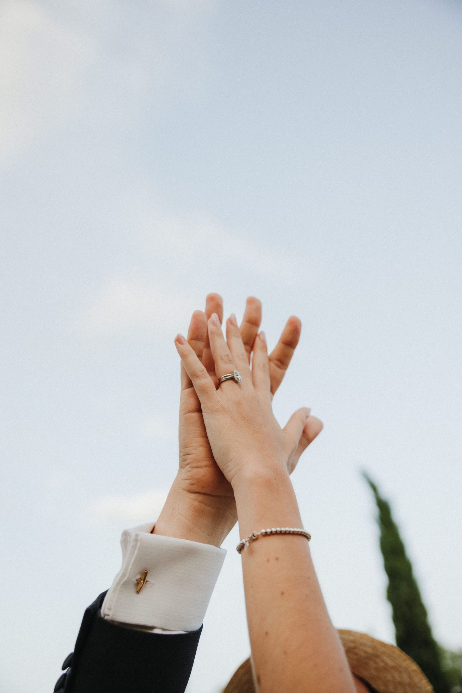 Close up of hands giving high fives against a light blue sky.