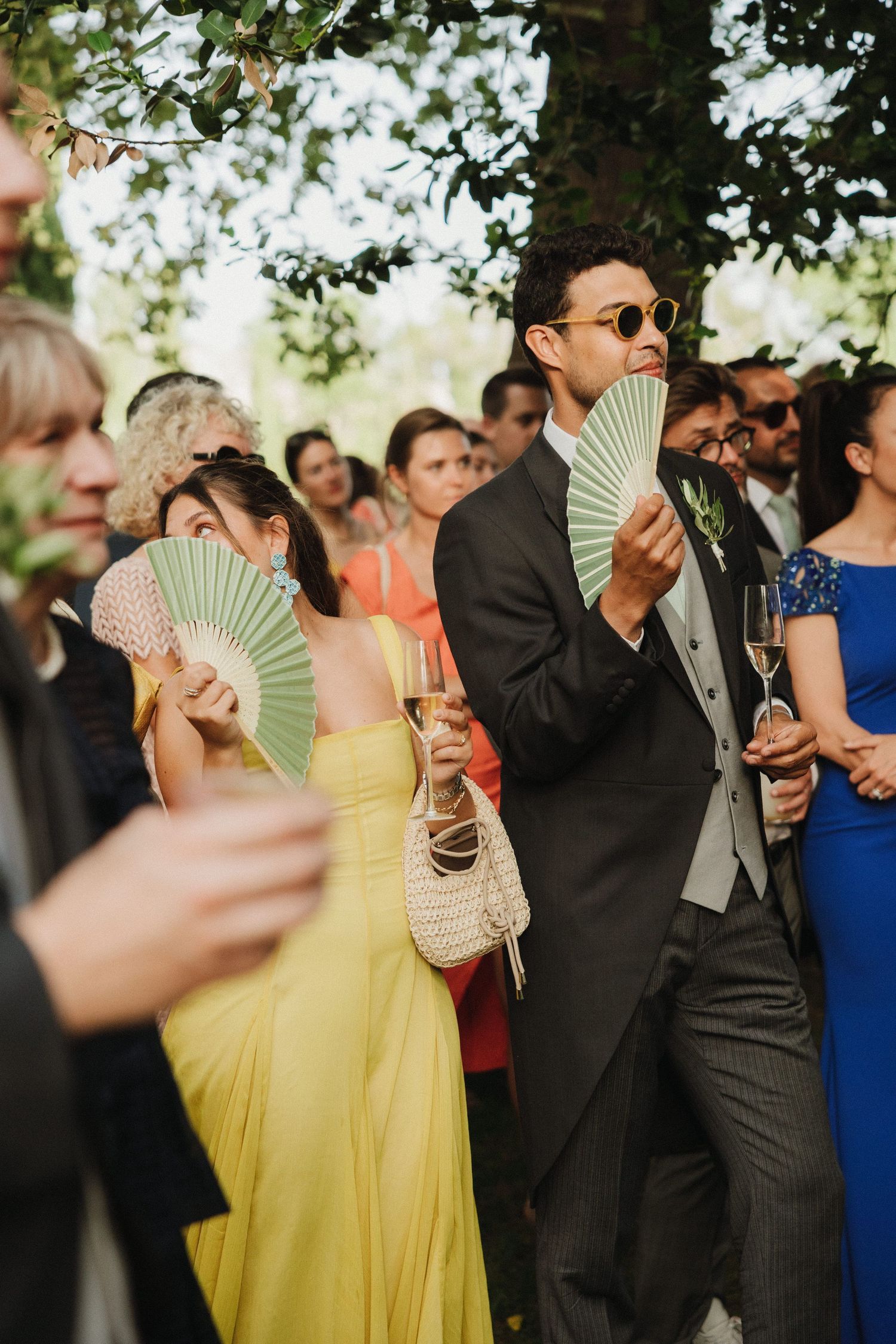 Wedding guests cooling off with decorative fans during an outdoor summer celebration.