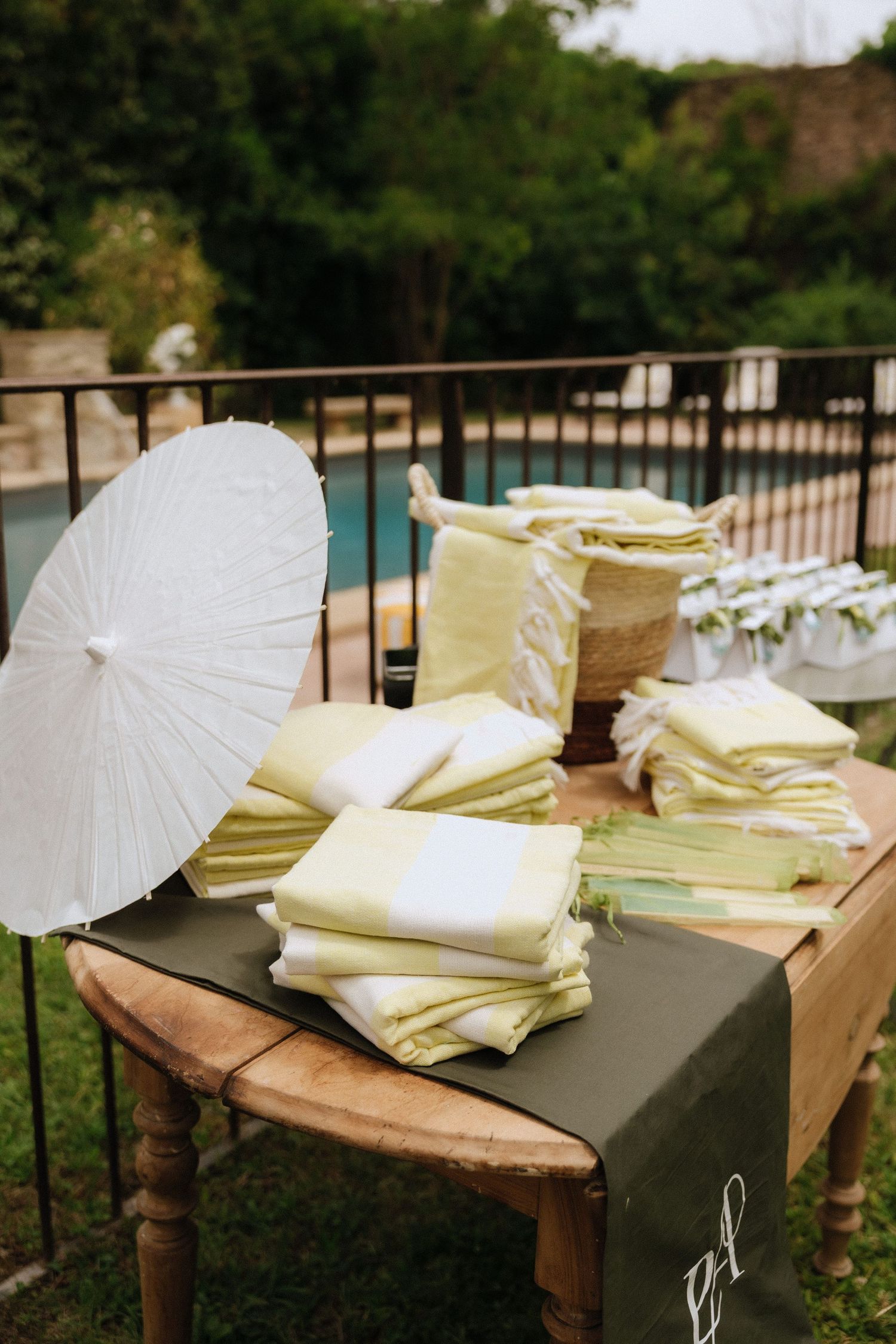 White paper parasols and wedding programs arranged on a rustic wooden table at an outdoor venue.