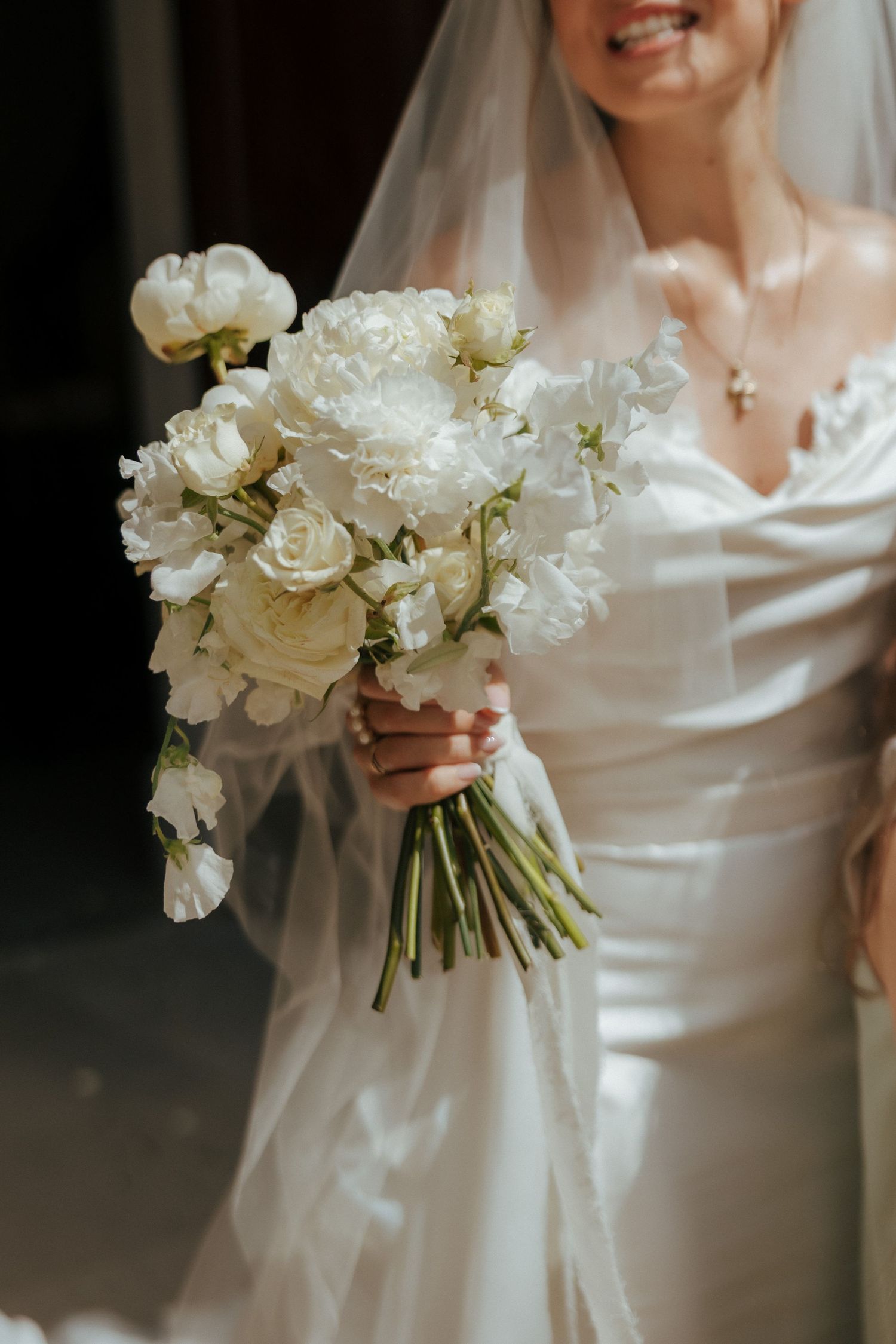 Classic white peony and rose bridal bouquet held against silk wedding dress.