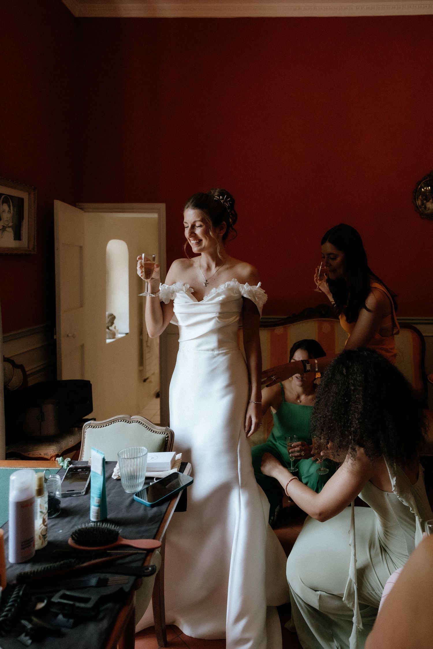 Wedding preparation scene with bridesmaids helping the bride get ready in a room with red walls.