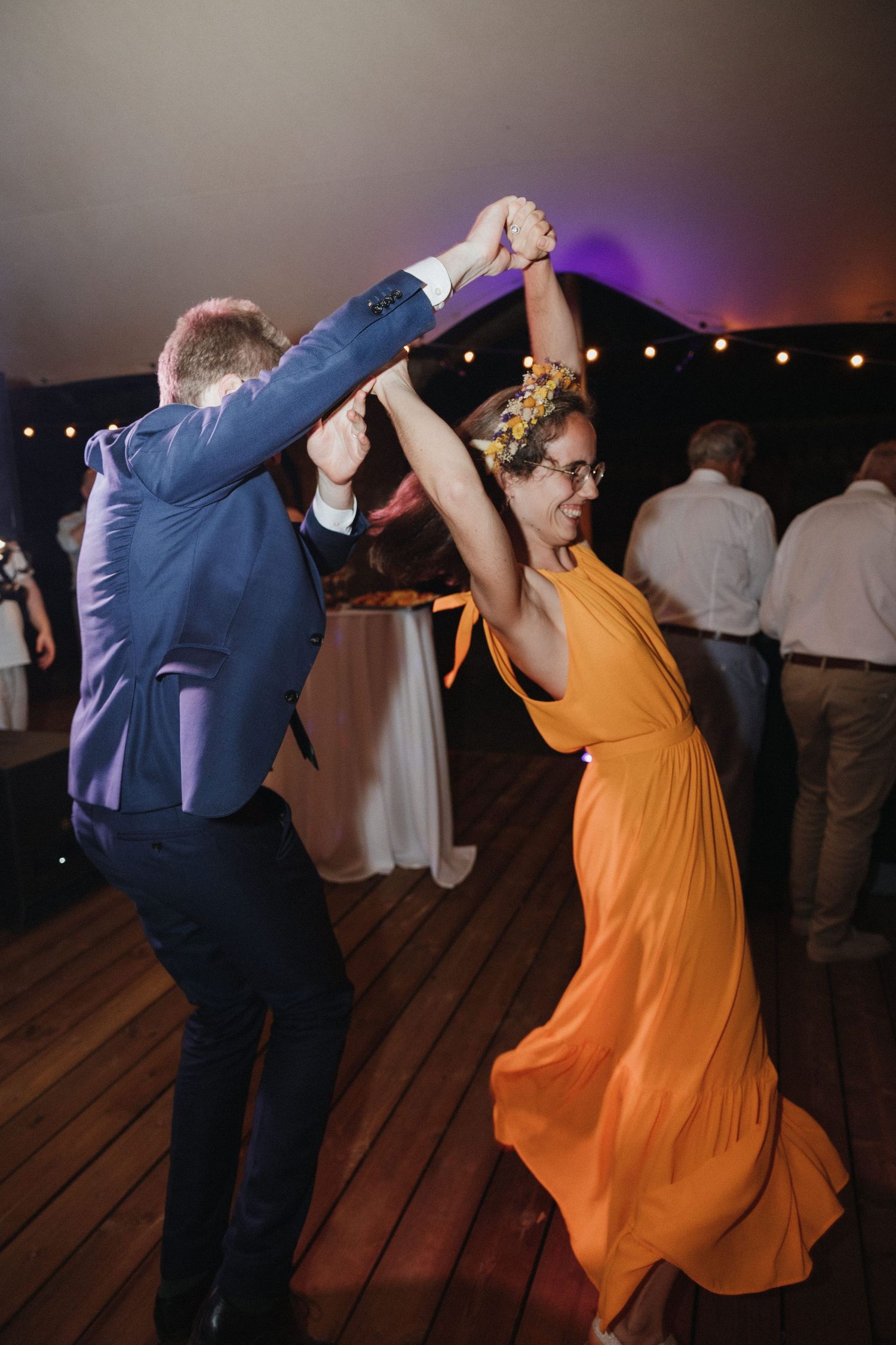 Dancers in formal attire twirling energetically on a wooden dance floor at an evening reception.