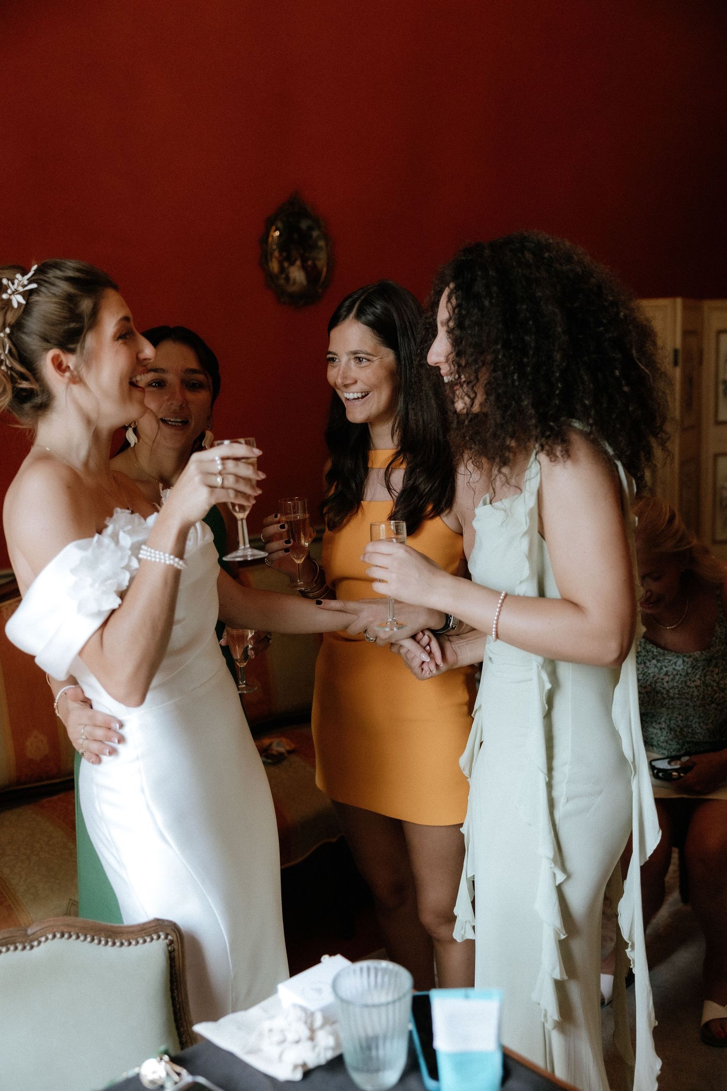 Bridesmaids in white dresses laughing and celebrating together during wedding preparations.