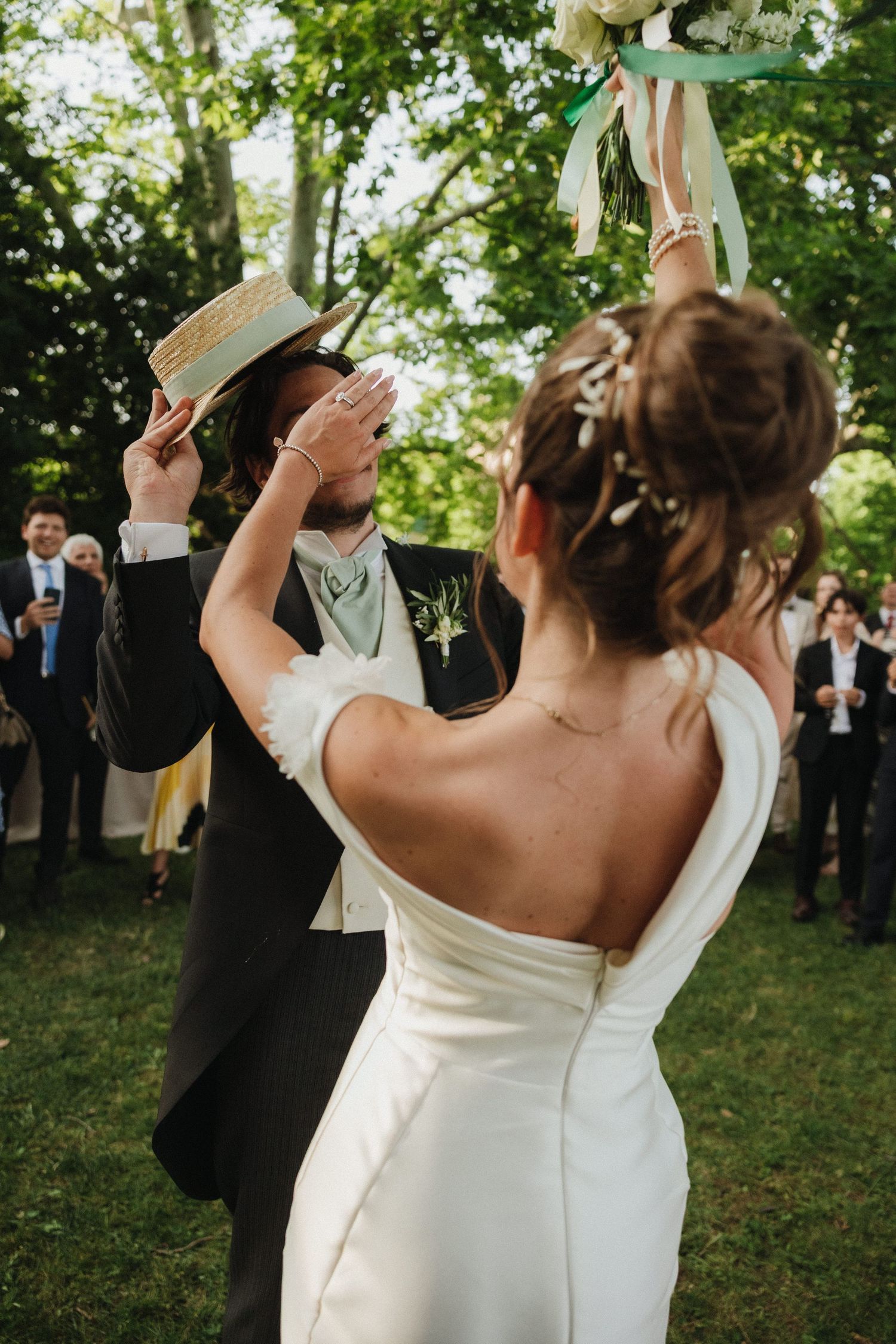 A couple shares a joyful moment during their wedding bouquet toss in an outdoor garden setting.