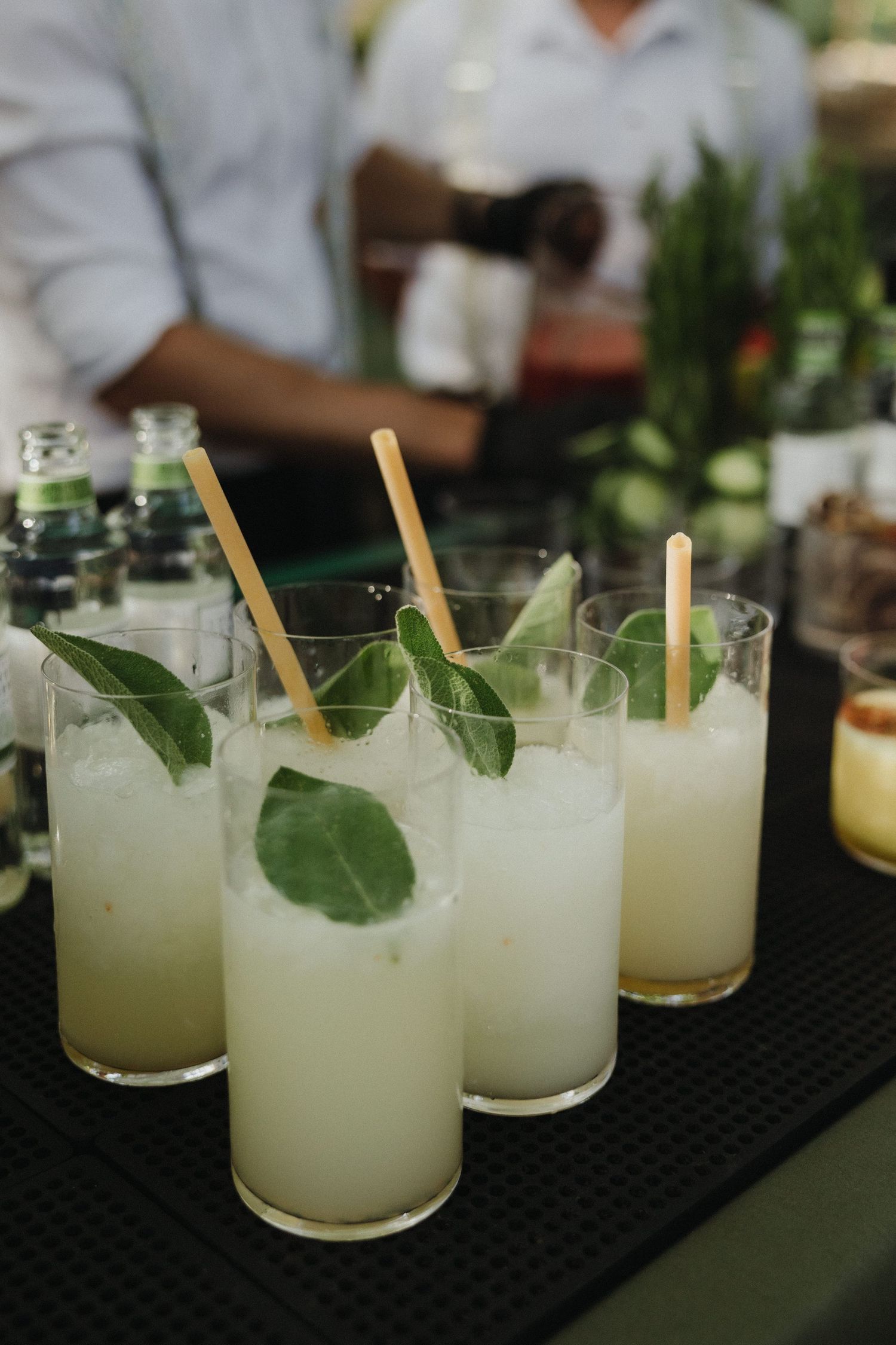 Refreshing cocktails garnished with herbs and bamboo straws served on a black bar mat.