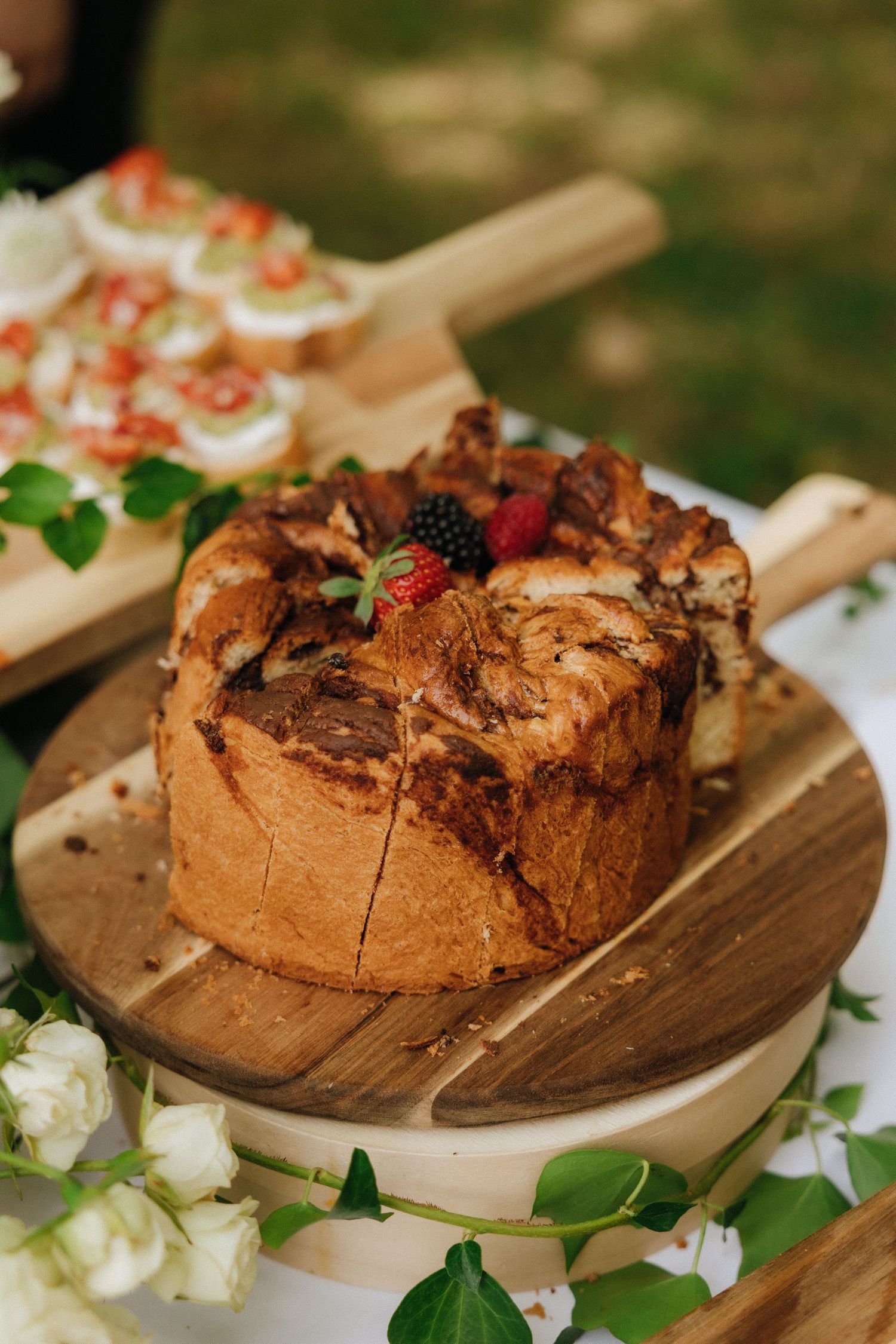 Rustic wedding cake decorated with berries and flowers displayed on wooden serving board.
