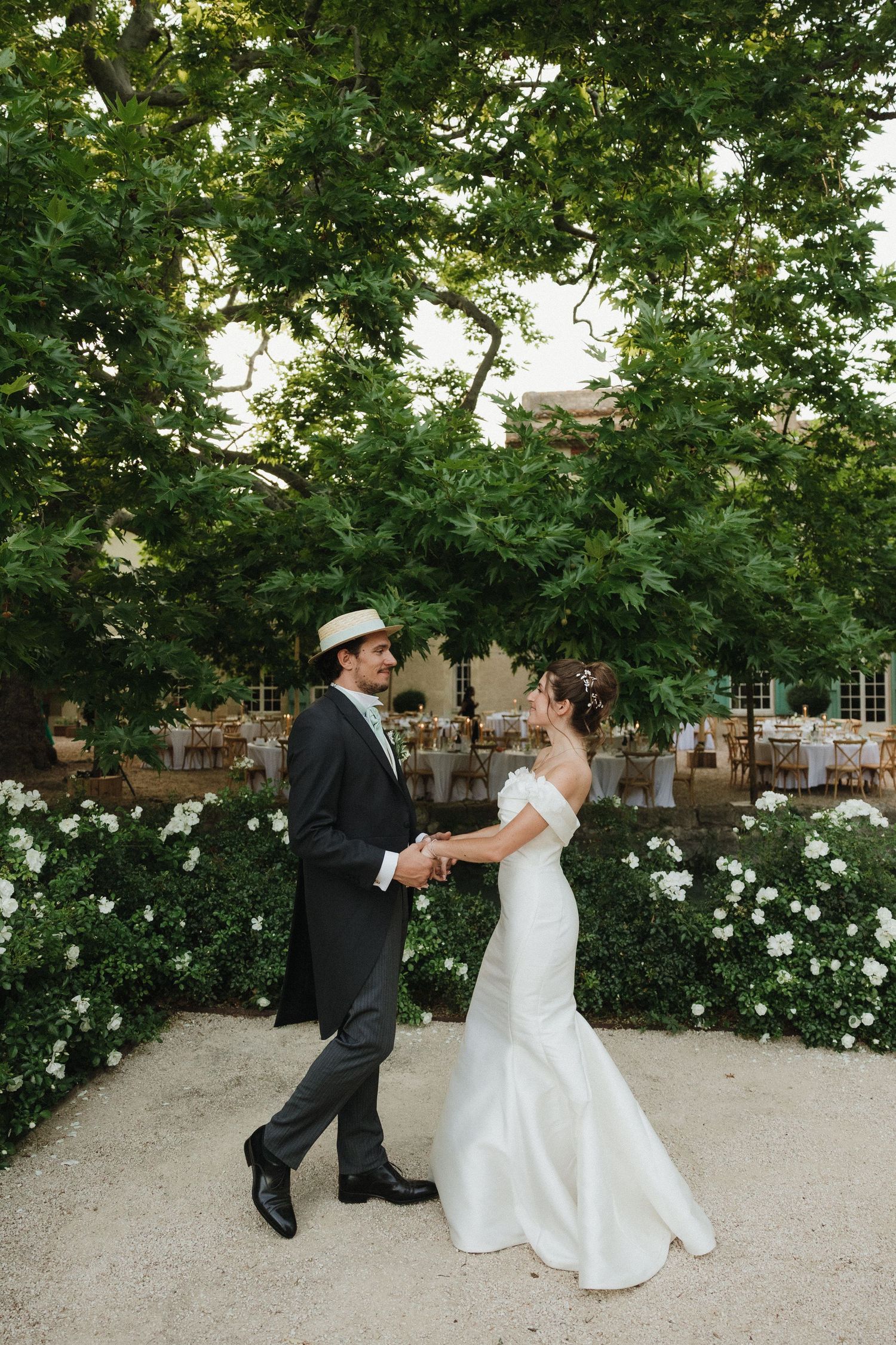 Couple dancing playfully on a garden path surrounded by blooming white roses and greenery.