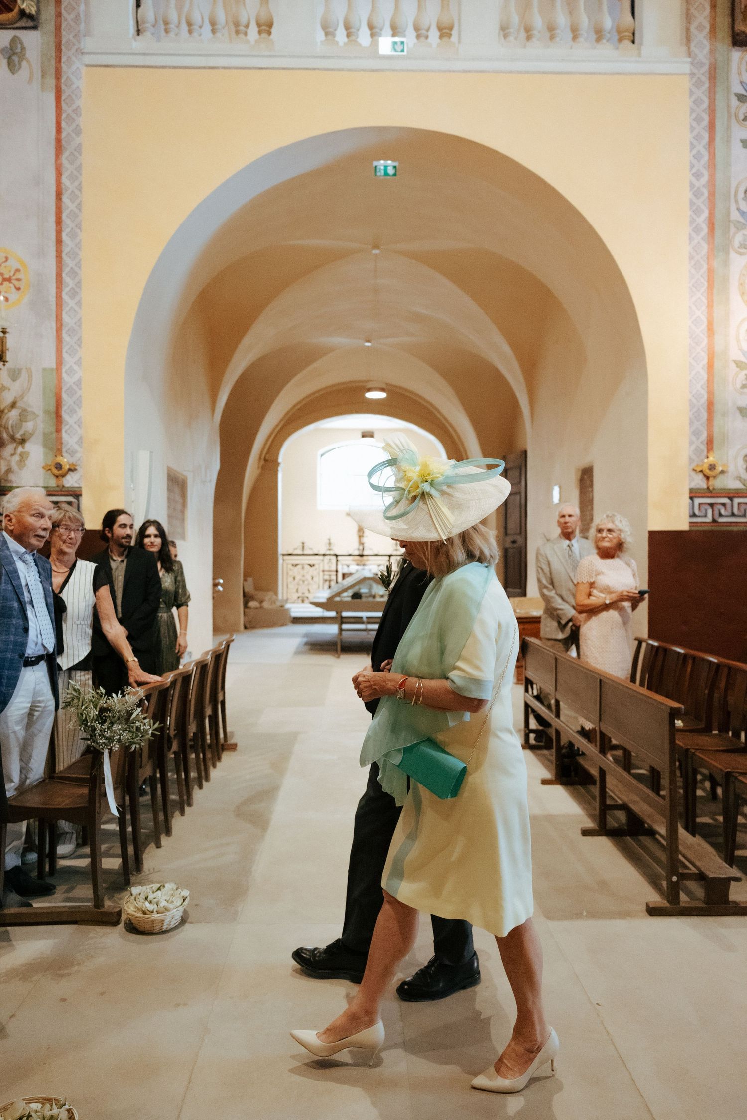Wedding guests mingling in elegant arched church hallway with ornate architectural details.
