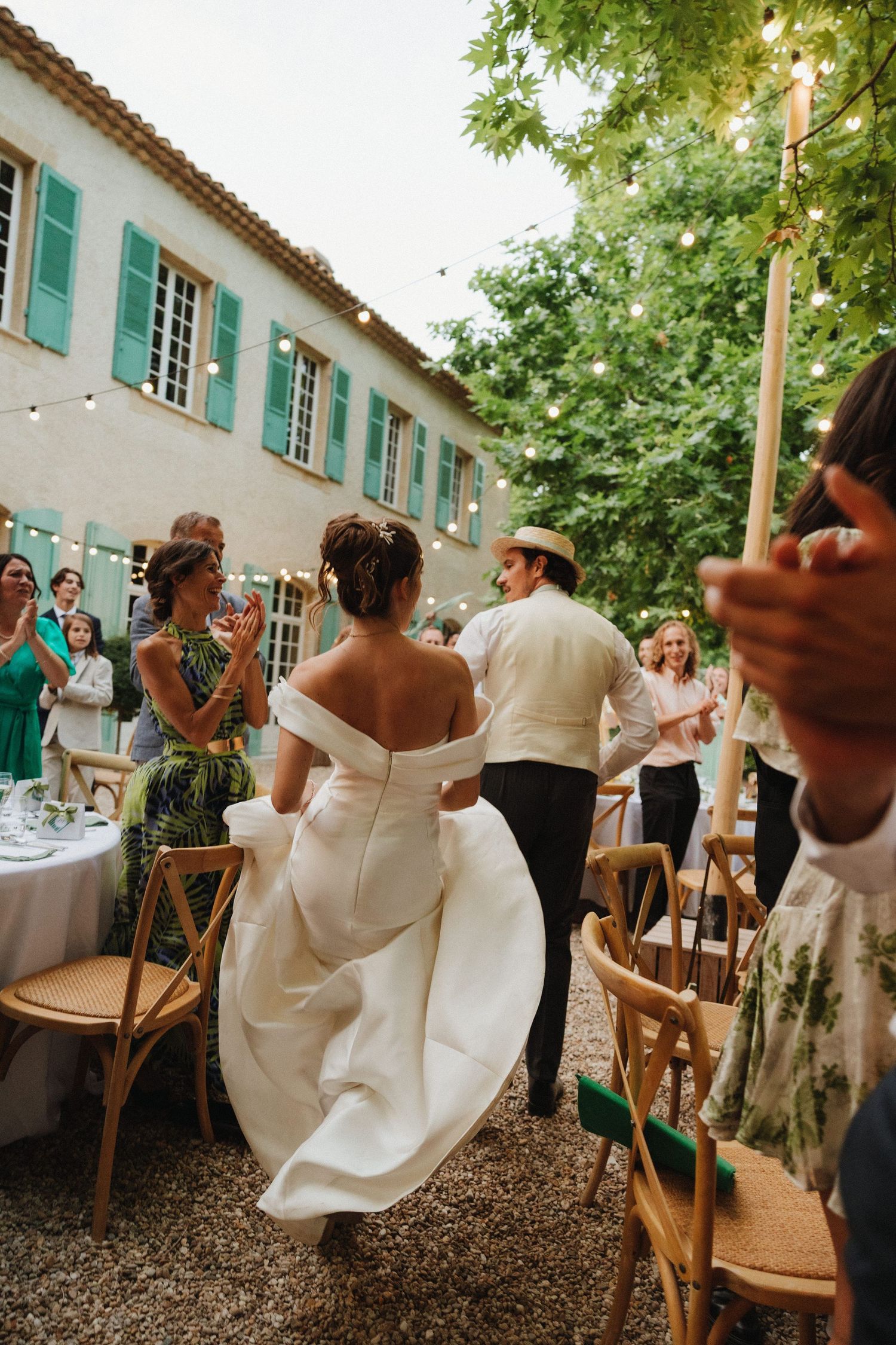 Wedding guests dance and celebrate at an outdoor reception with turquoise shutters and garden setting.