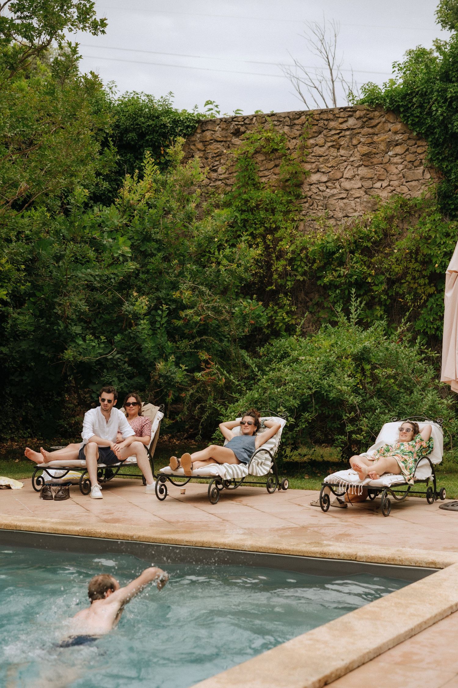 Time-lapse sequence showing people jumping into a swimming pool beside a stone wall and garden.