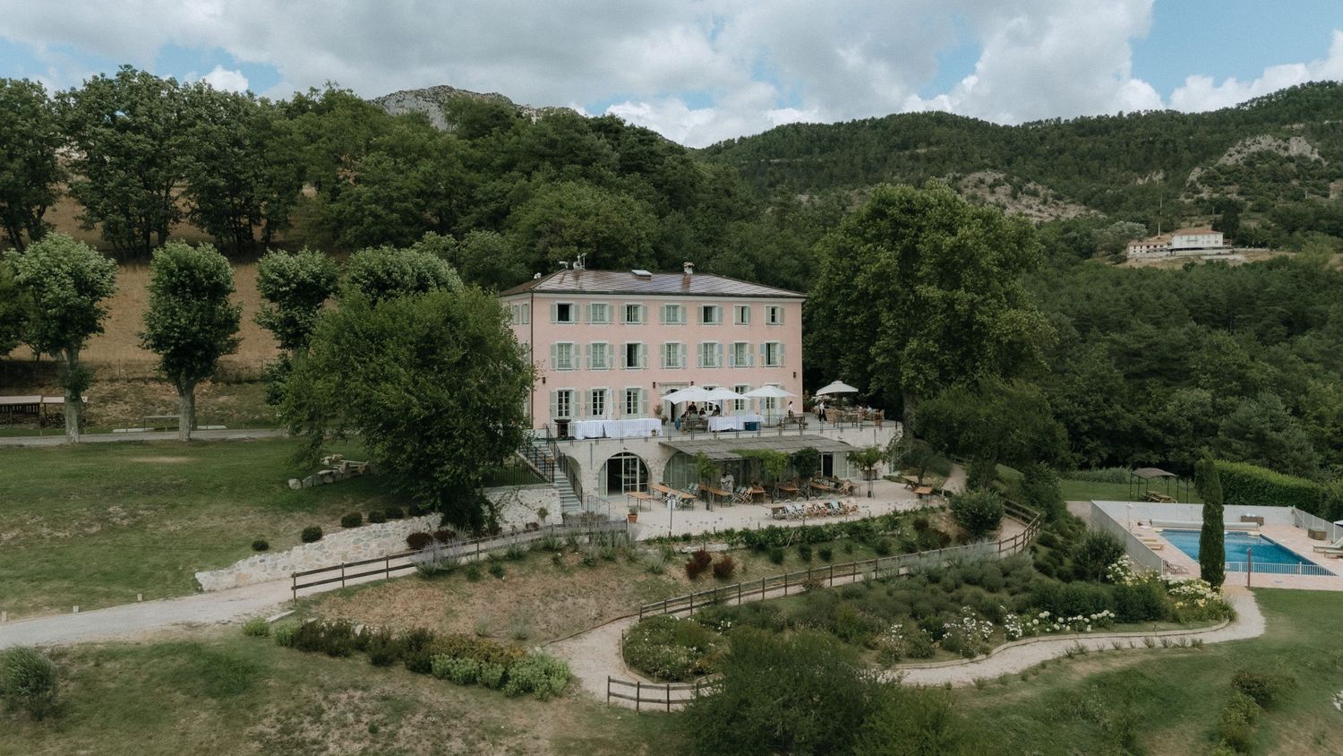 Panoramic view of stone villas nestled in rolling green hills with swimming pools and Mediterranean landscaping.